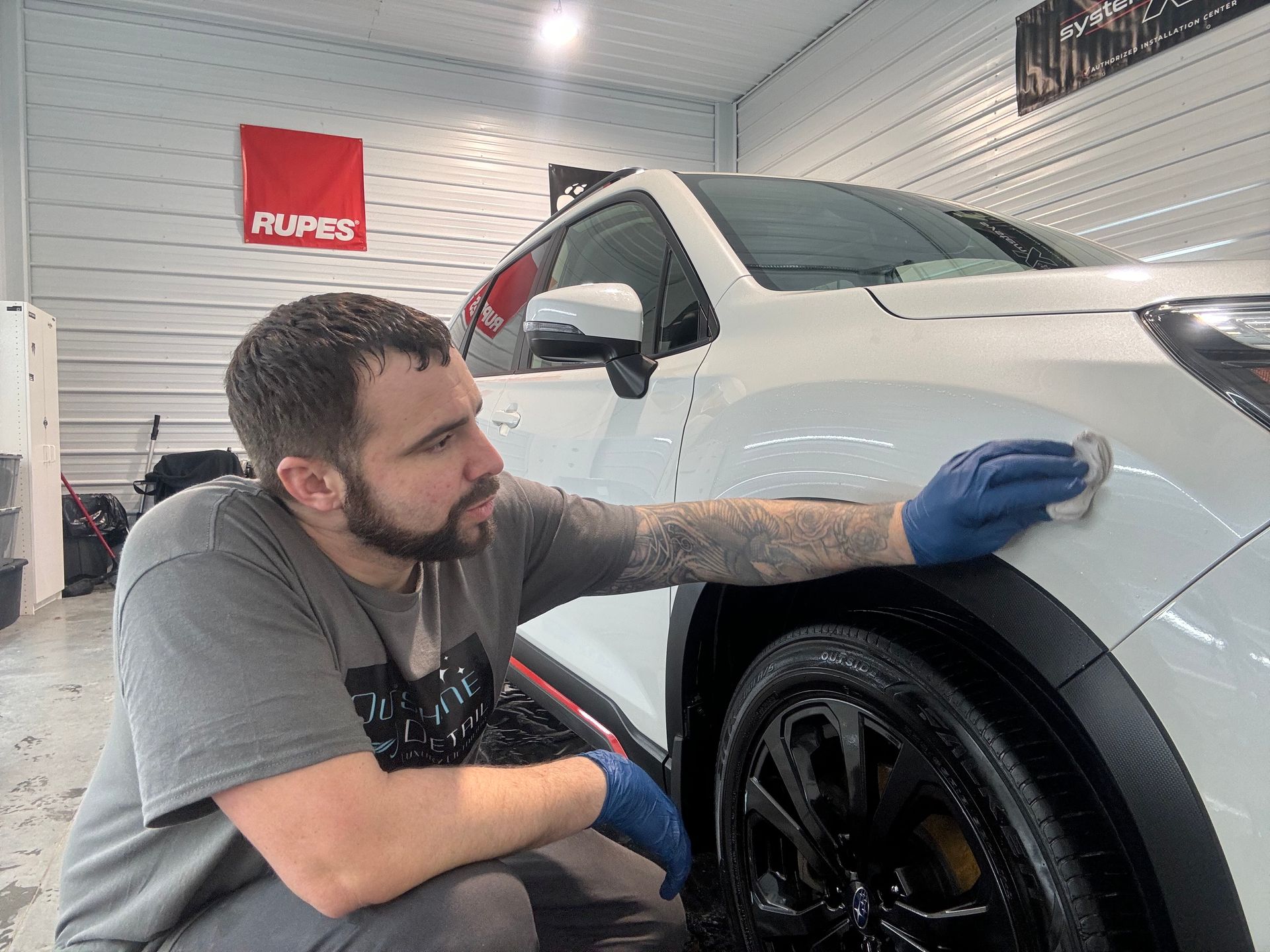 A man is kneeling down next to a white car in a garage.