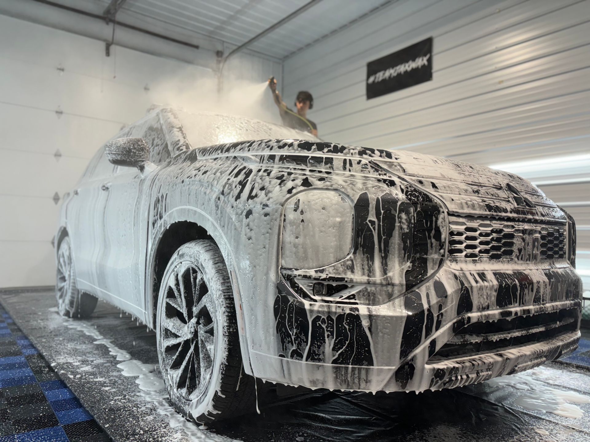 Person spraying foamy car wash solution on a black SUV in a garage.