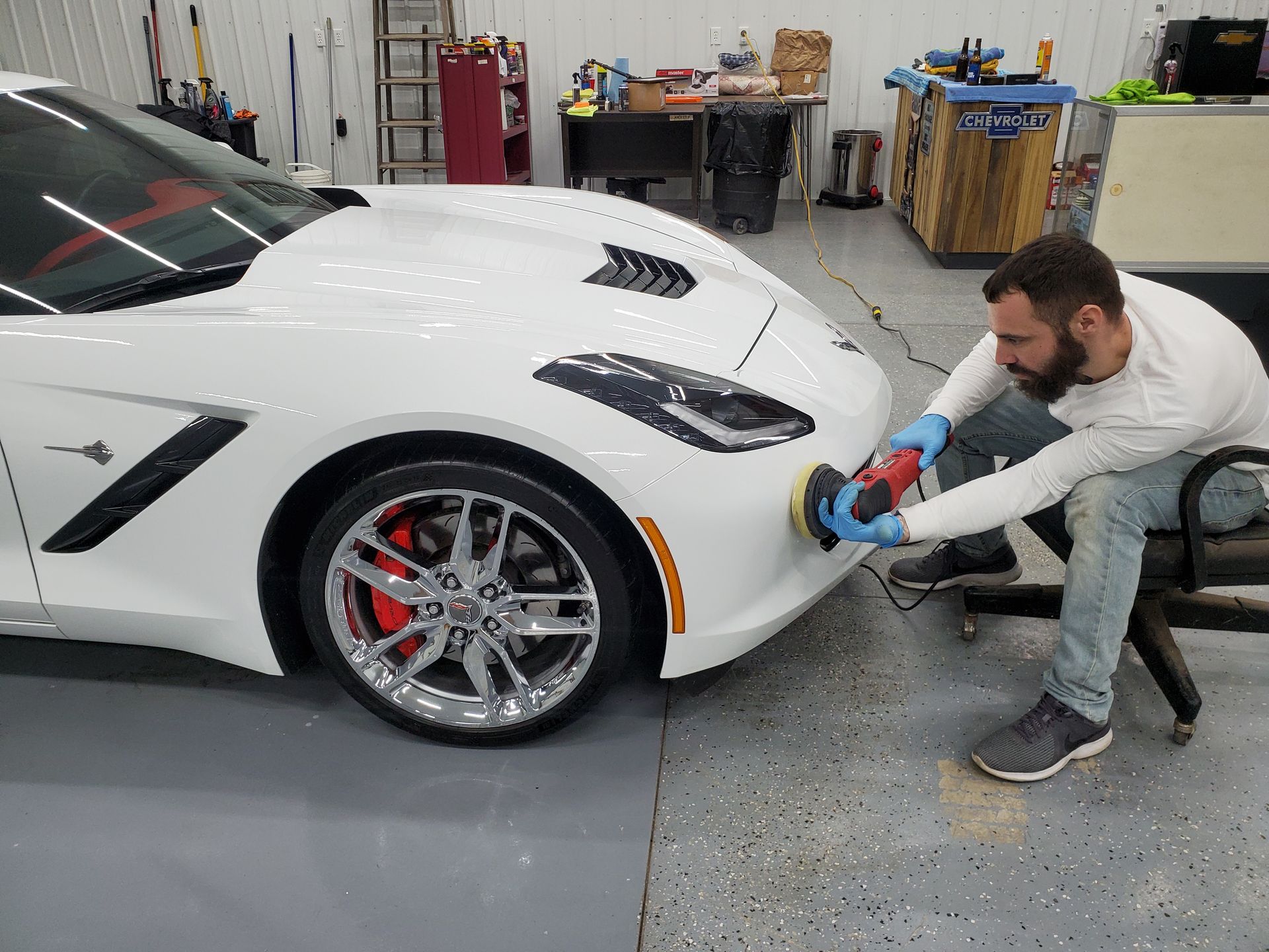 A man is polishing a white sports car in a garage.