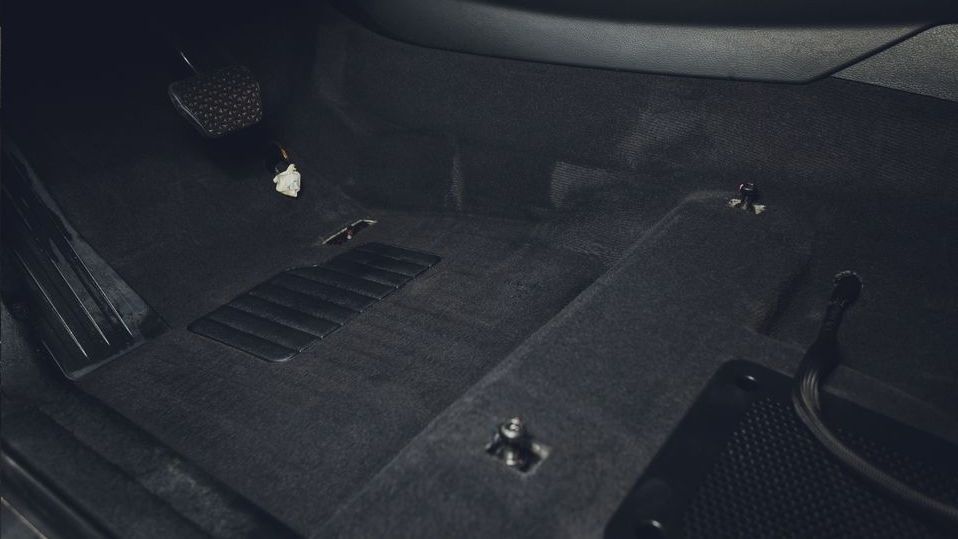 The inside of a car with a black carpet and a brake pedal.
