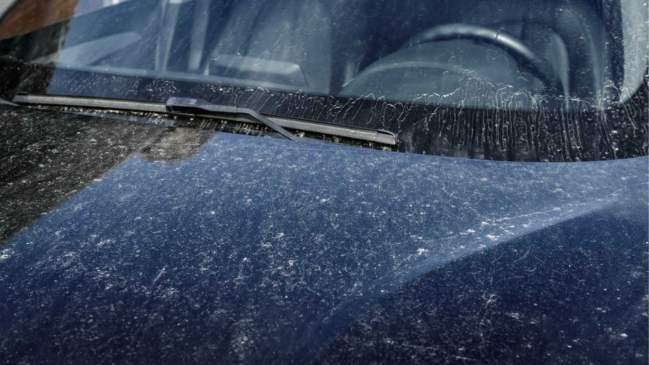 A close up of a dirty car with snow on the windshield and hood.