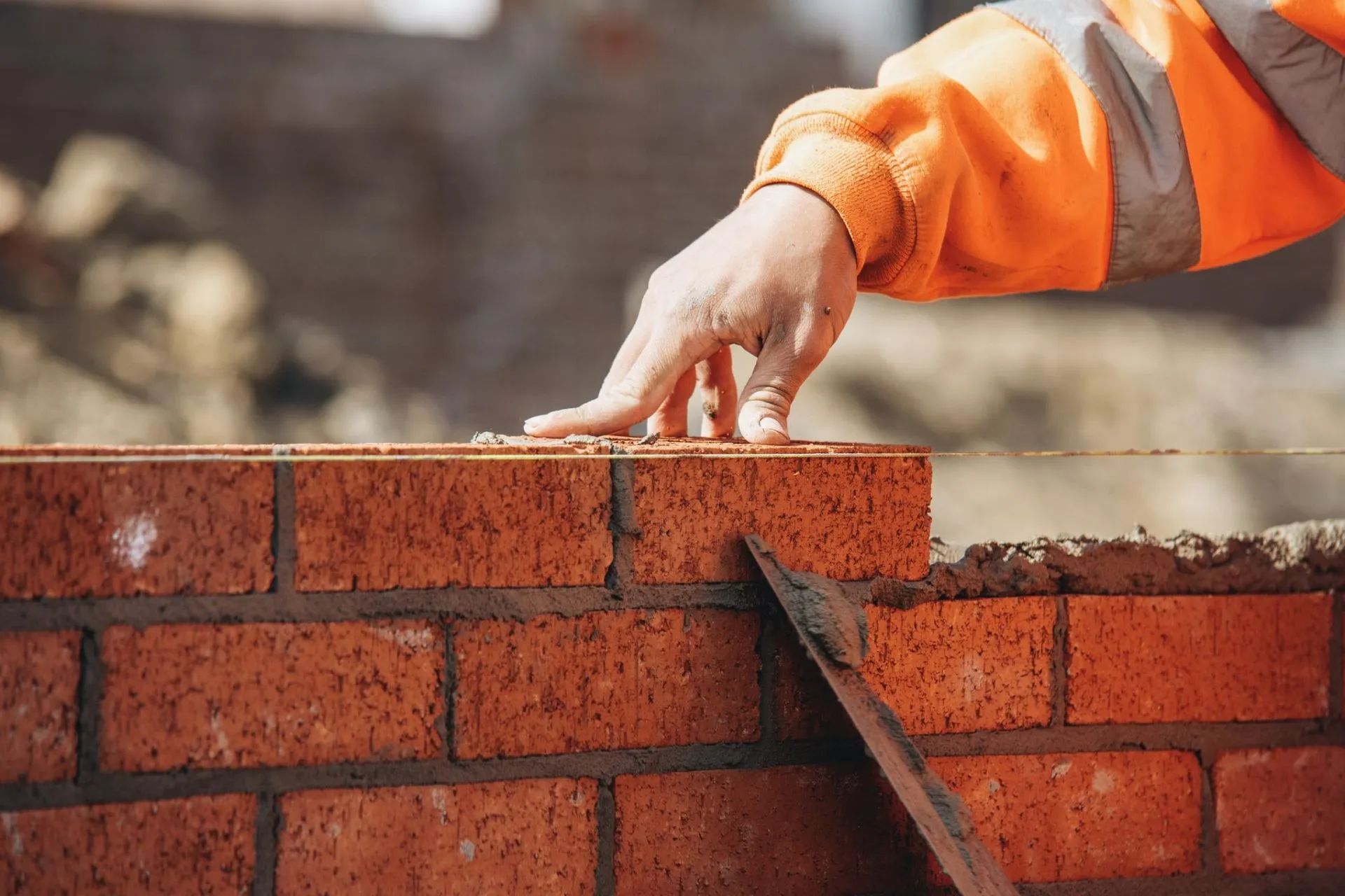 Bricklayer building a red brick wall with mortar on a construction site