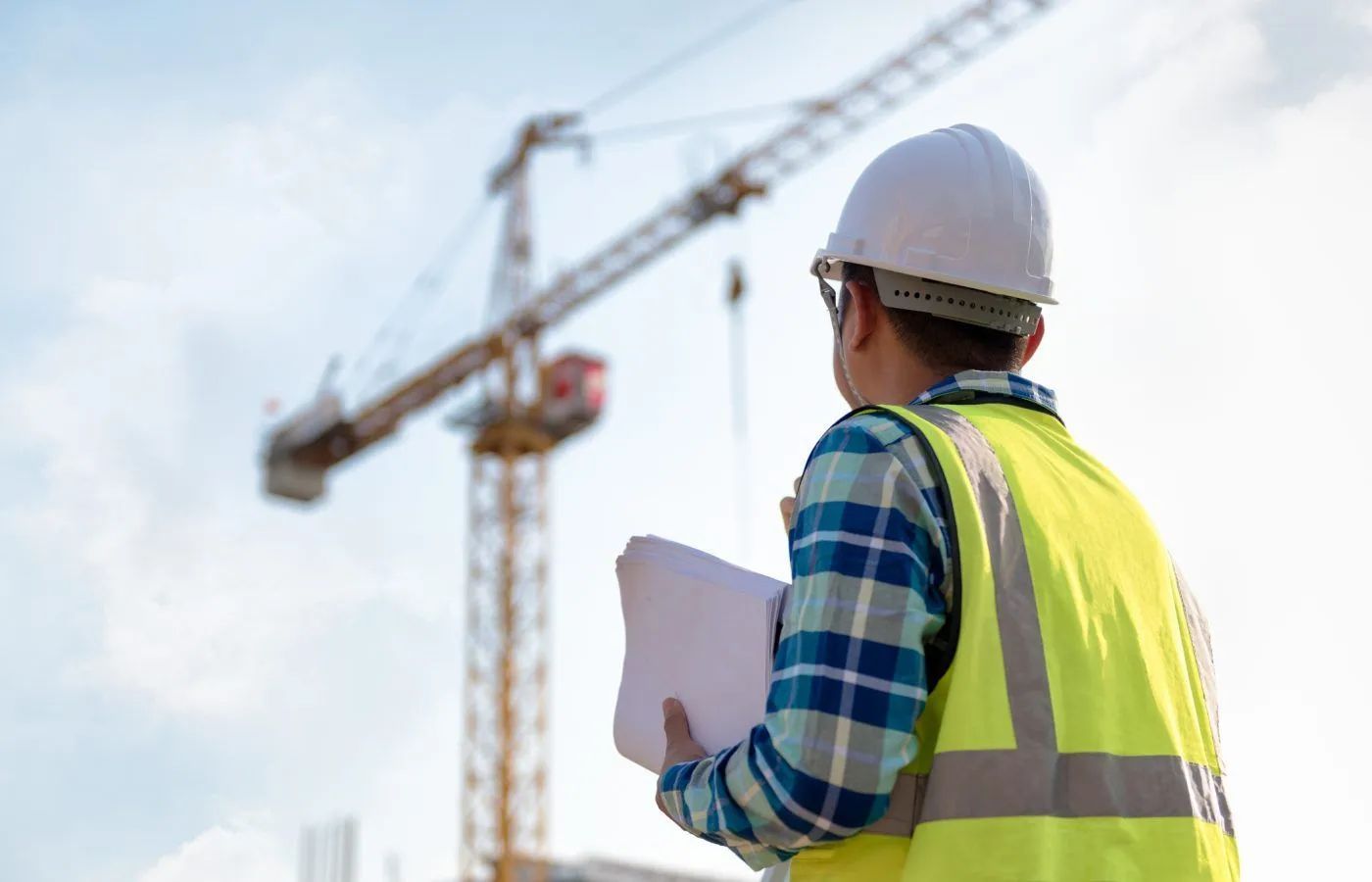 Builder in high-vis vest and hard hat reviewing plans on construction site