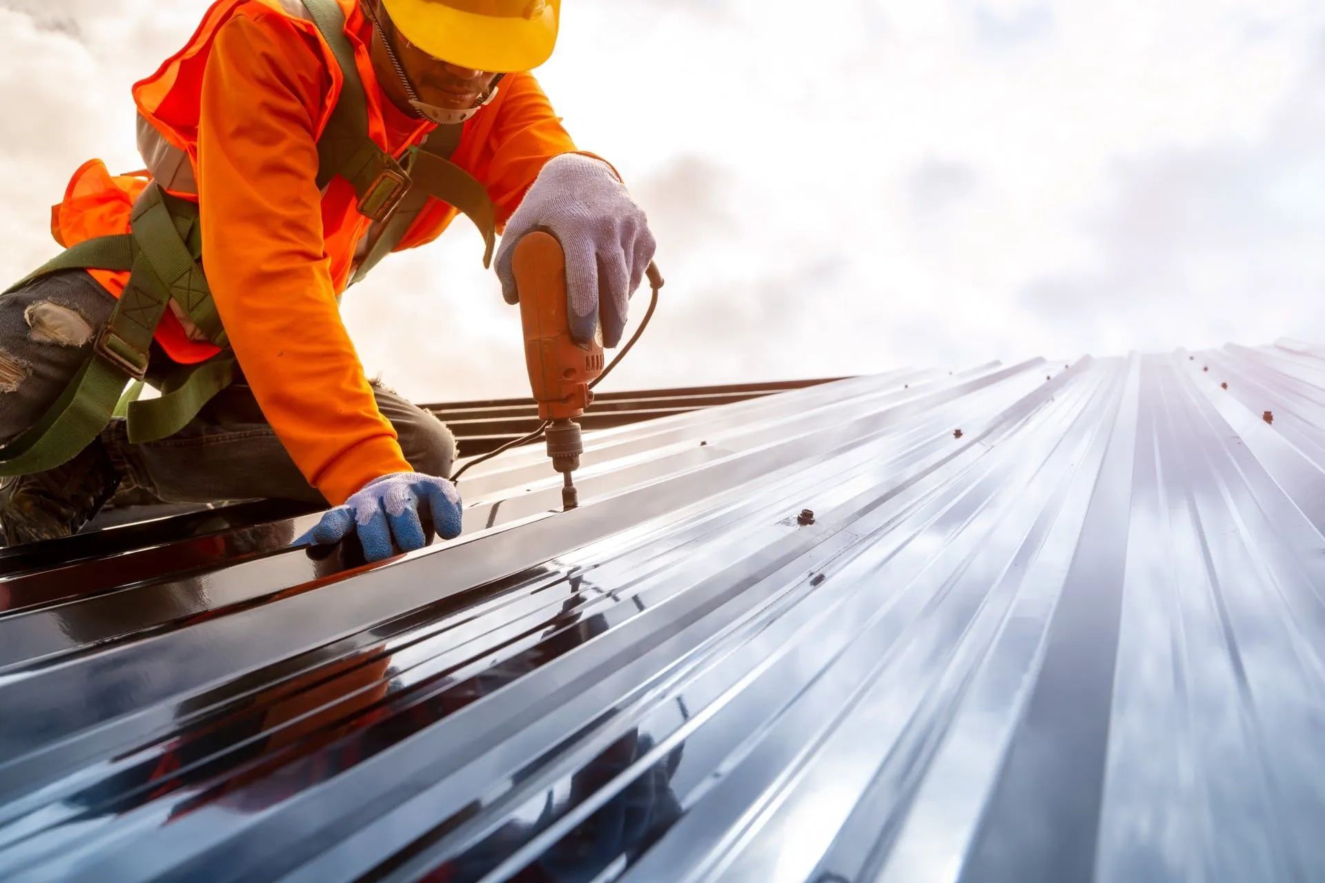 Worker performing building maintenance by securing roofing panels with a drill