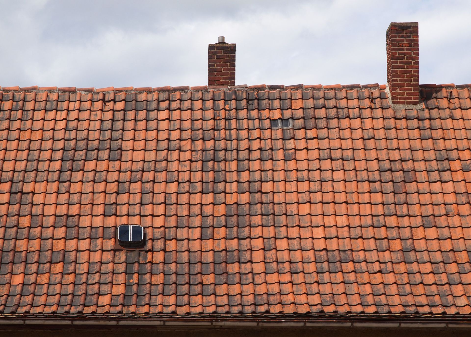 the roof of a house with red tiles and two chimneys .