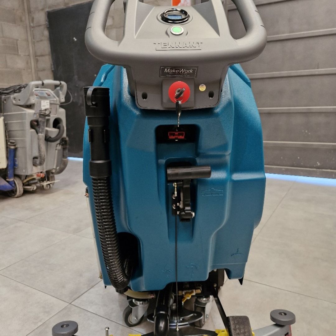 Una fregadora de pisos de color verde azulado y gris con mango, controles y llave, para uso en interiores.