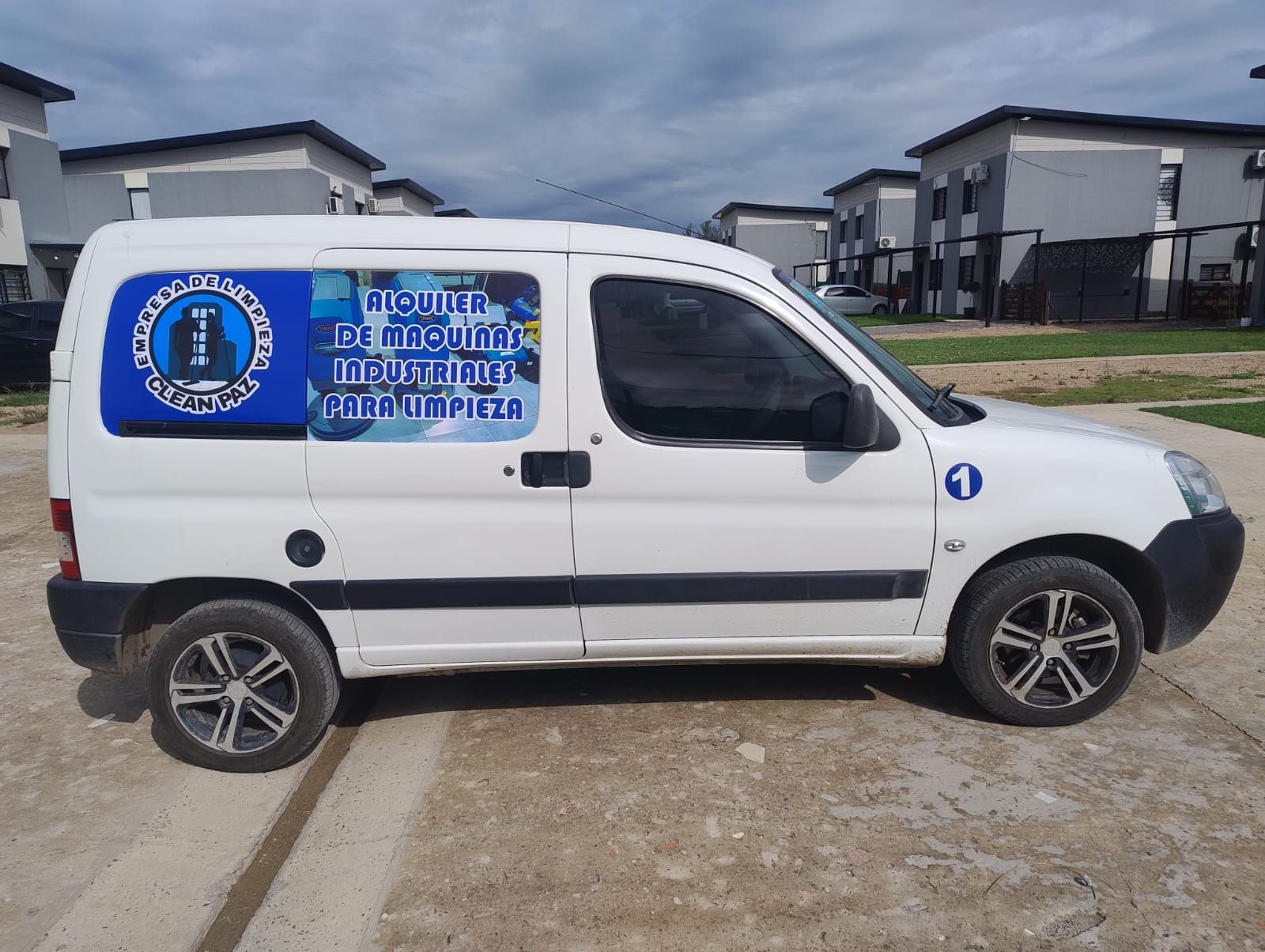 Furgoneta blanca con logo azul en el lateral, estacionada frente a casas adosadas.