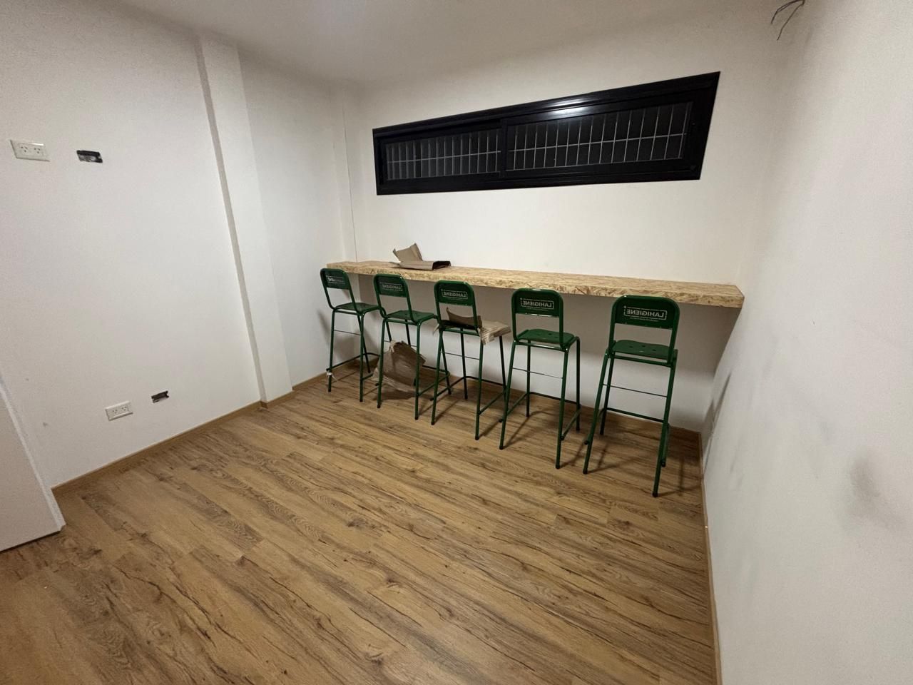 Una habitación con una barra de madera, sillas verdes y una ventana.