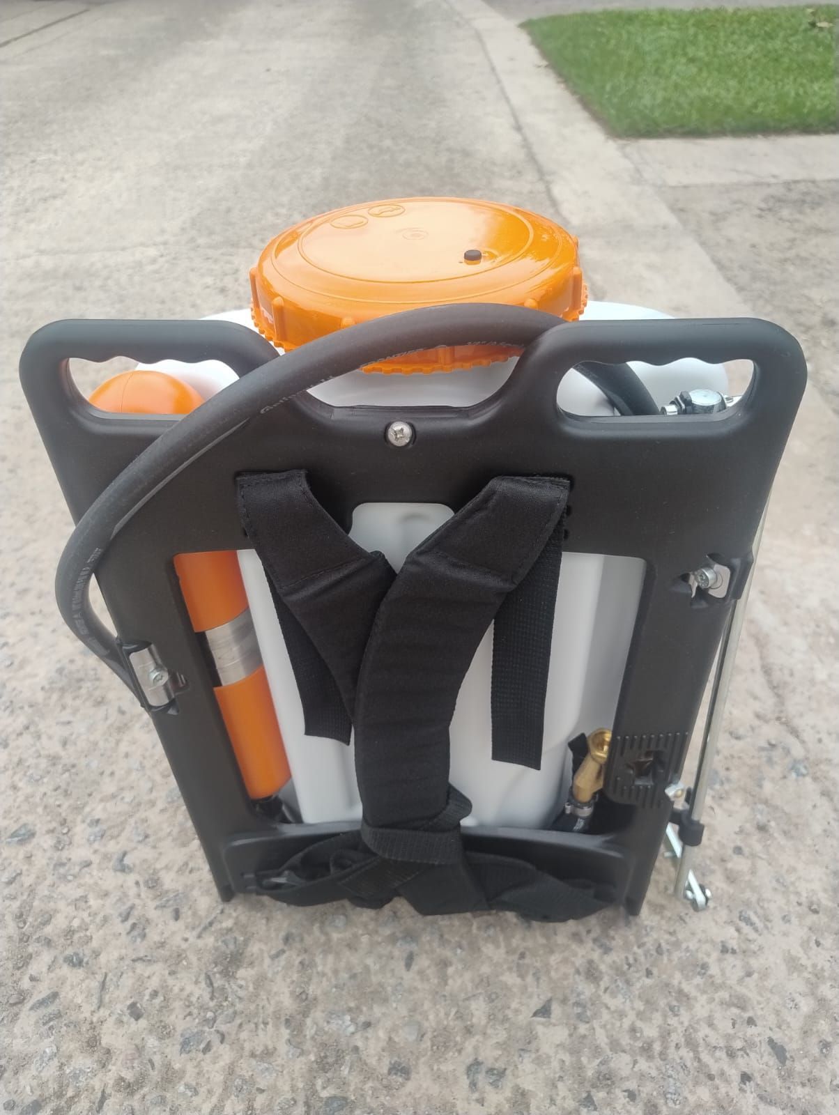 Pulverizador de mochila con componentes de color naranja y negro, correas negras, sobre superficie de hormigón.
