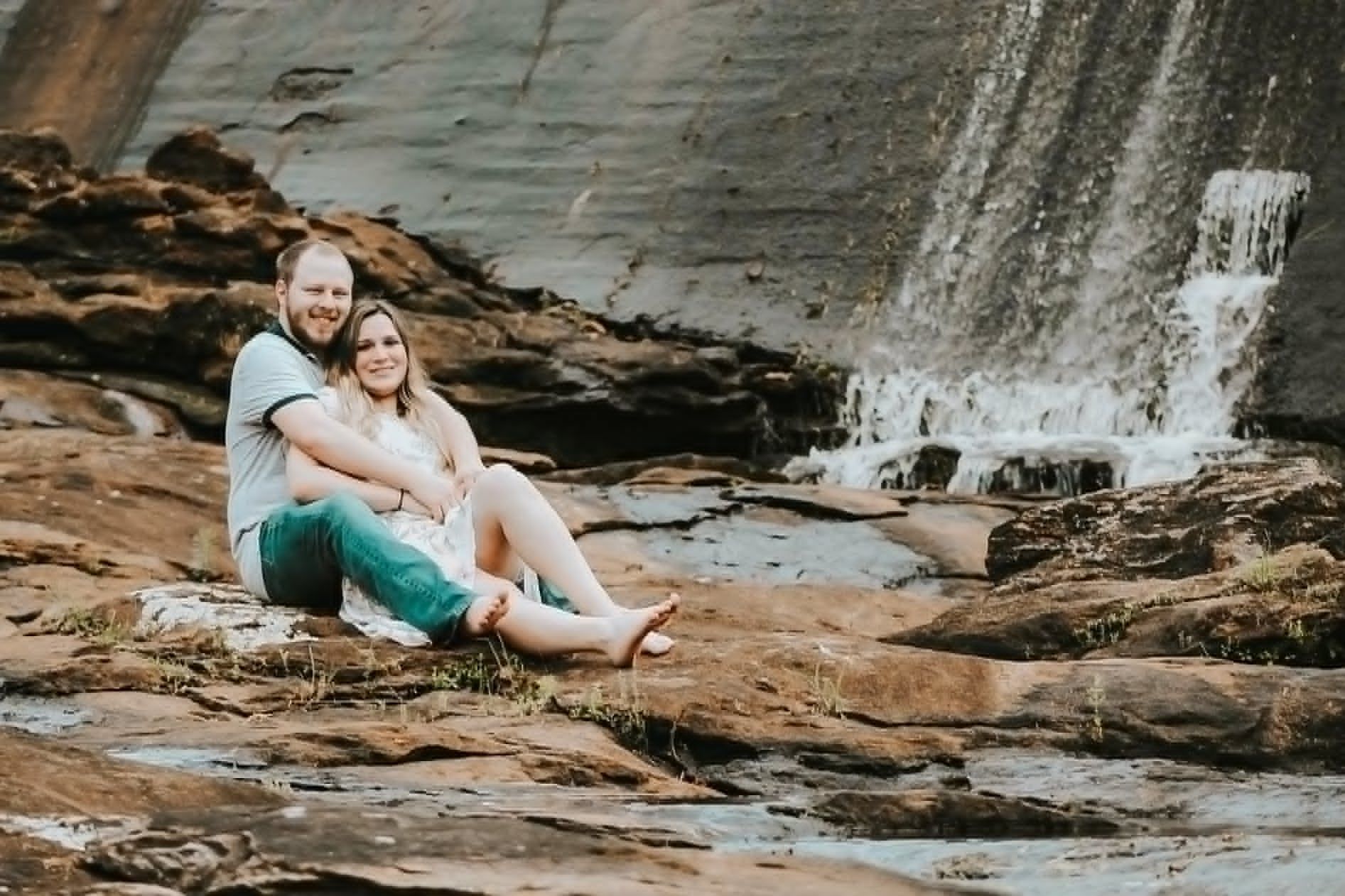 Couple sitting together on rocks near a waterfall during an engagement photography session in Newnan, GA.