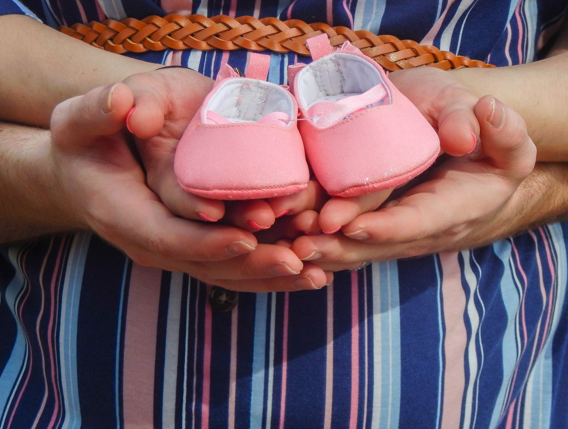 Parents holding small pink baby booties during a maternity portrait photoshoot