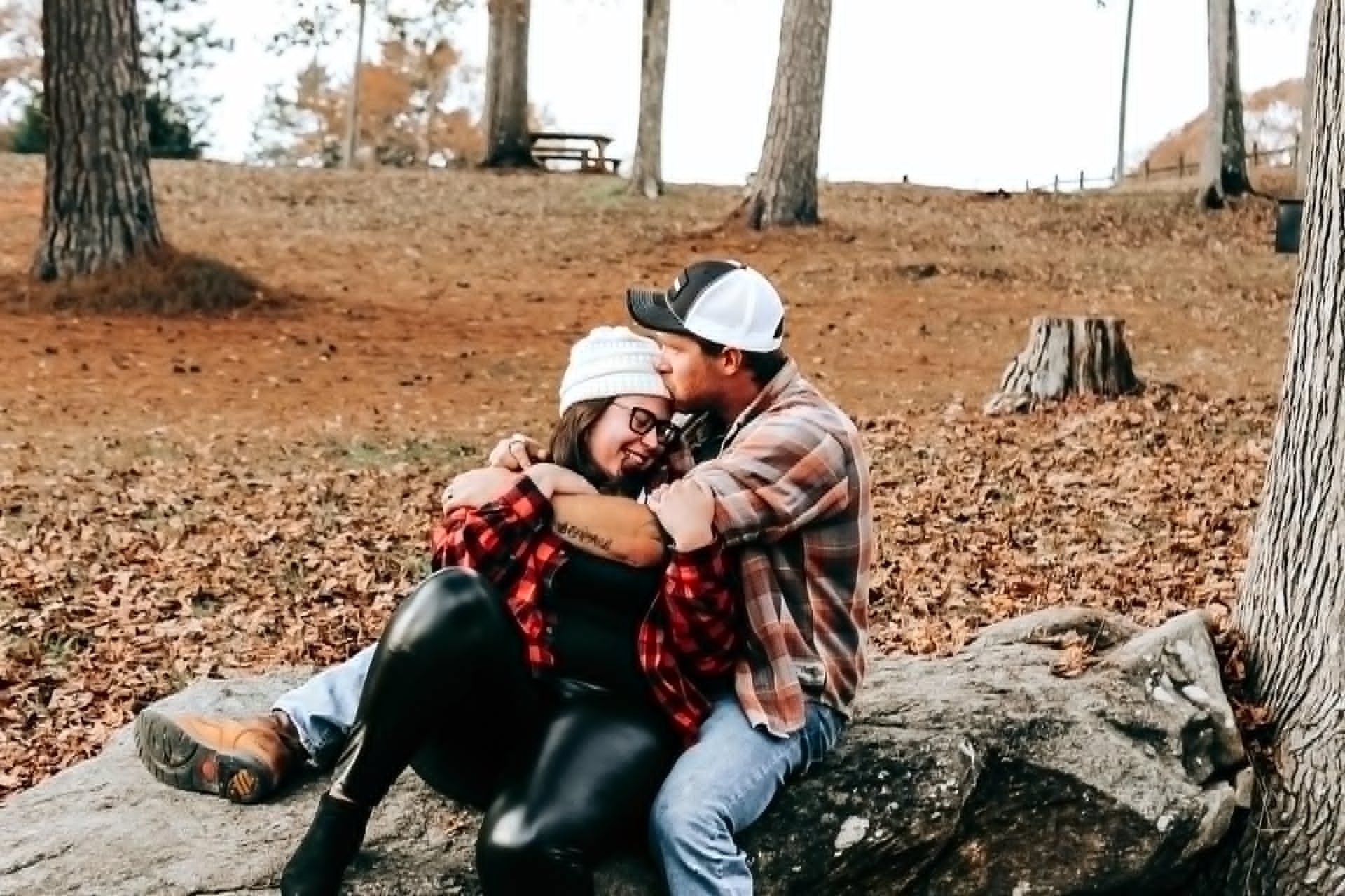 Couple sitting together on a fallen tree trunk in the woods for an engagement photo session in Newnan, GA.