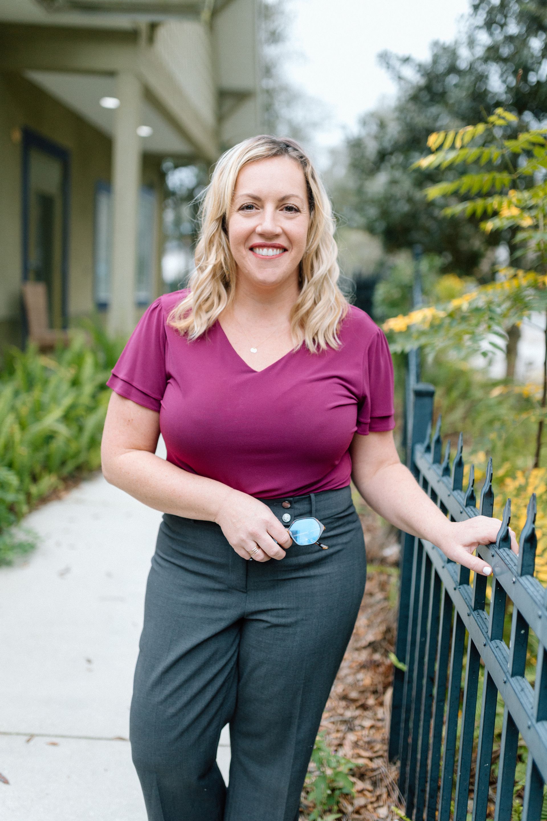 A woman in a tan coat is smiling for the camera in a park.