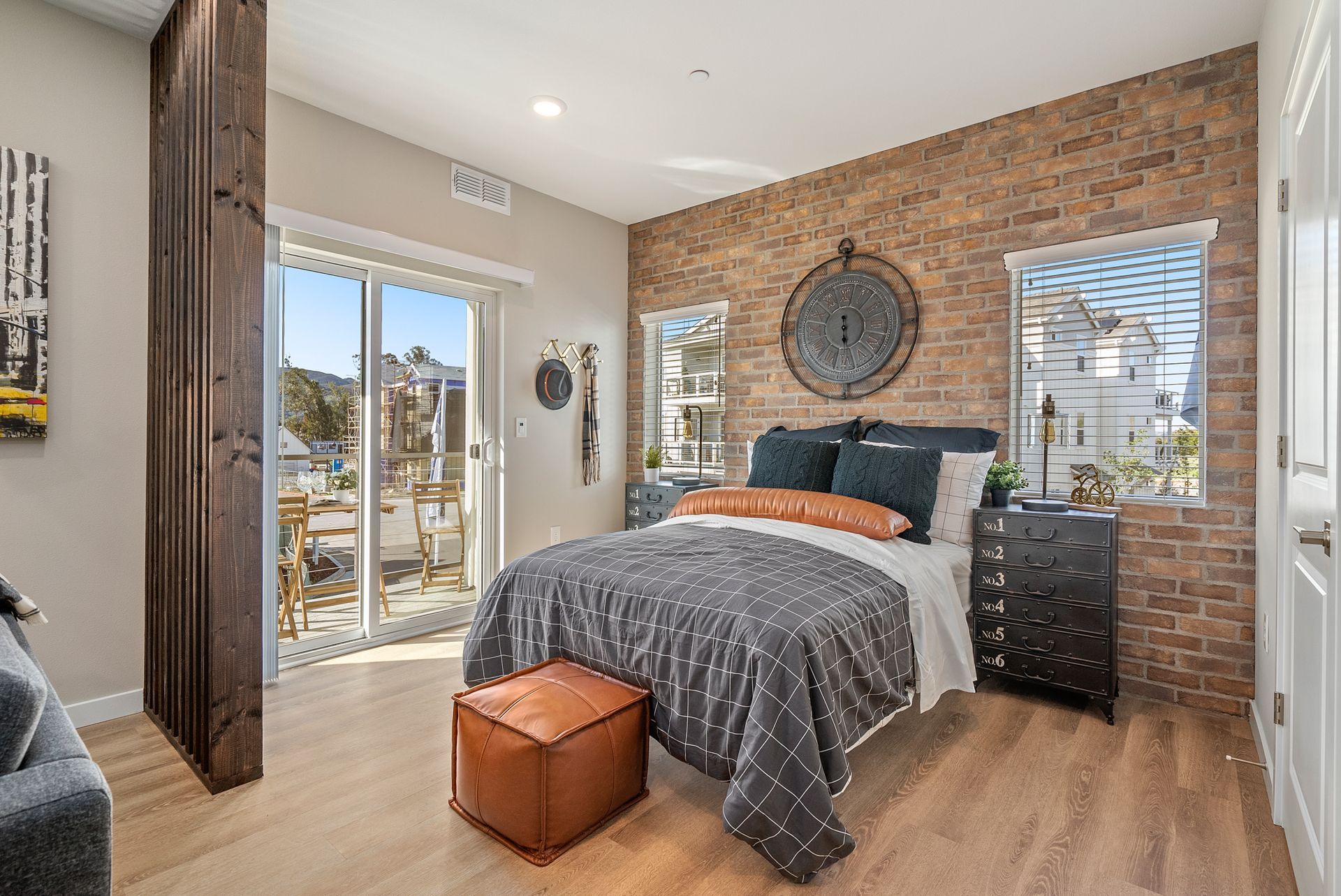 Bedroom with brick wall, sliding door to balcony, and leather ottoman.
