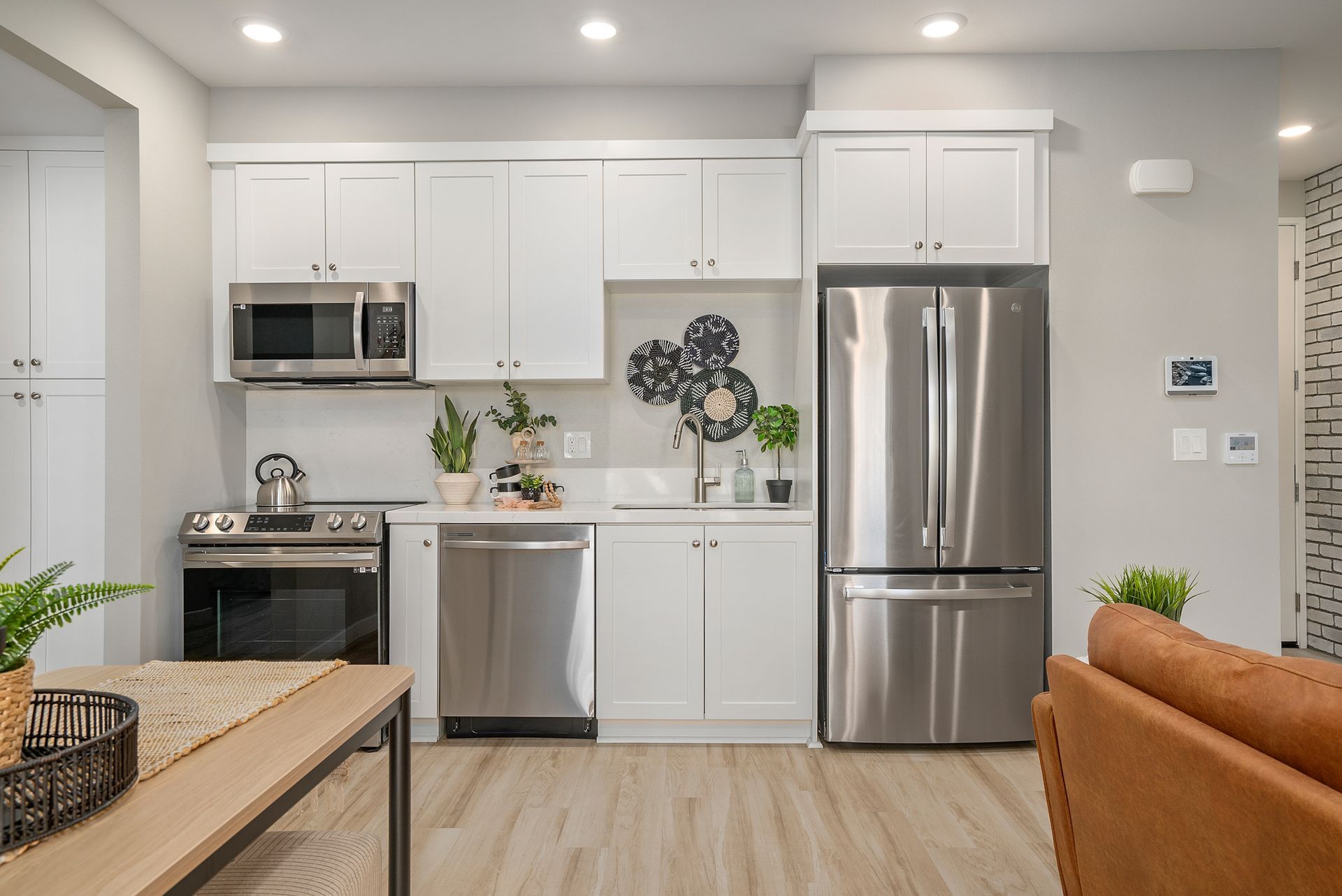 Modern white kitchen with stainless steel appliances, light wood floors, and minimalist decor.