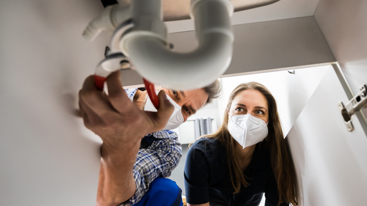 A man and a woman wearing masks are fixing a sink pipe.