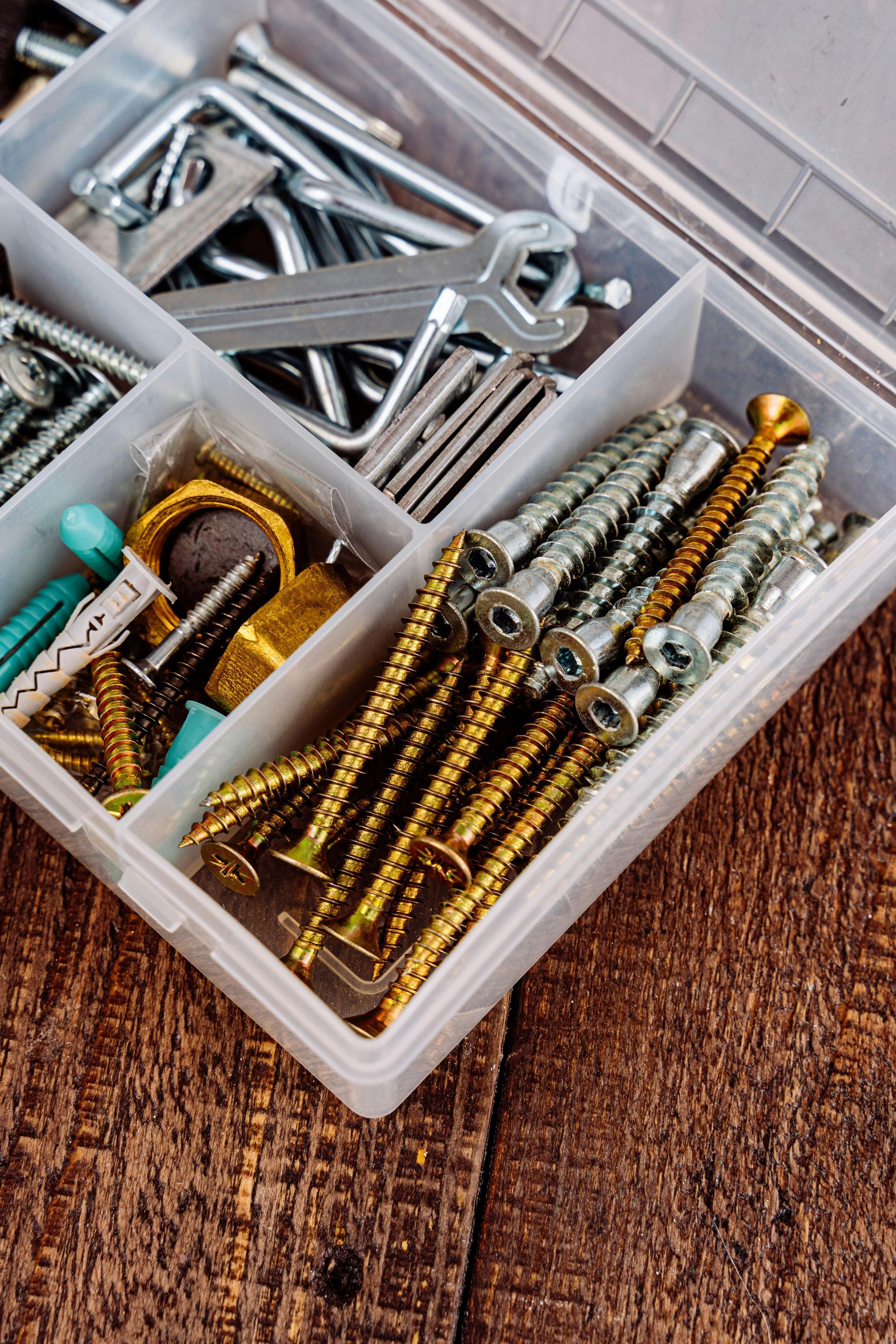 A plastic box filled with screws and wrenches on a wooden table.
