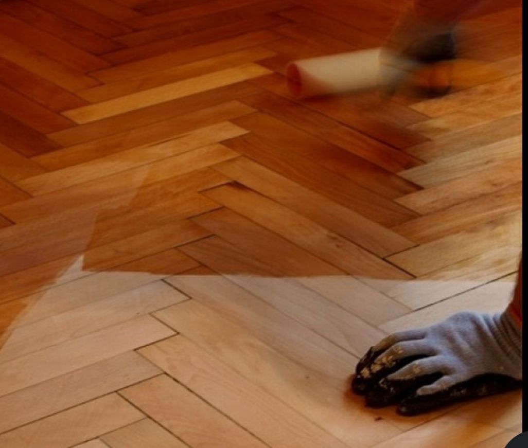 Una persona arrodillada sobre un piso de madera en espiga, usando una cinta métrica y un lápiz 