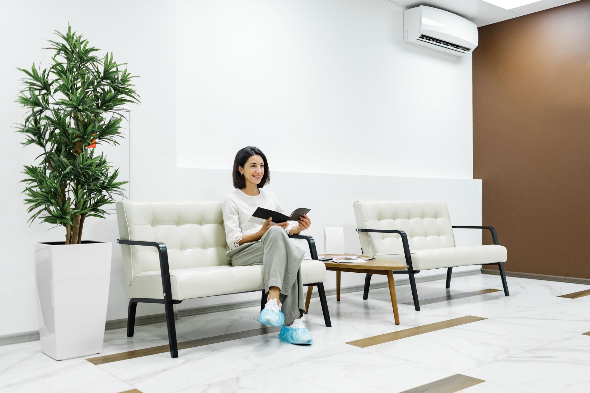 A woman is sitting on a couch in a waiting room reading a book.