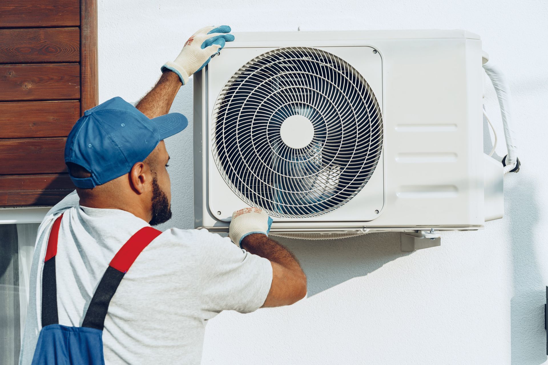 A man is installing an air conditioner on the side of a building.