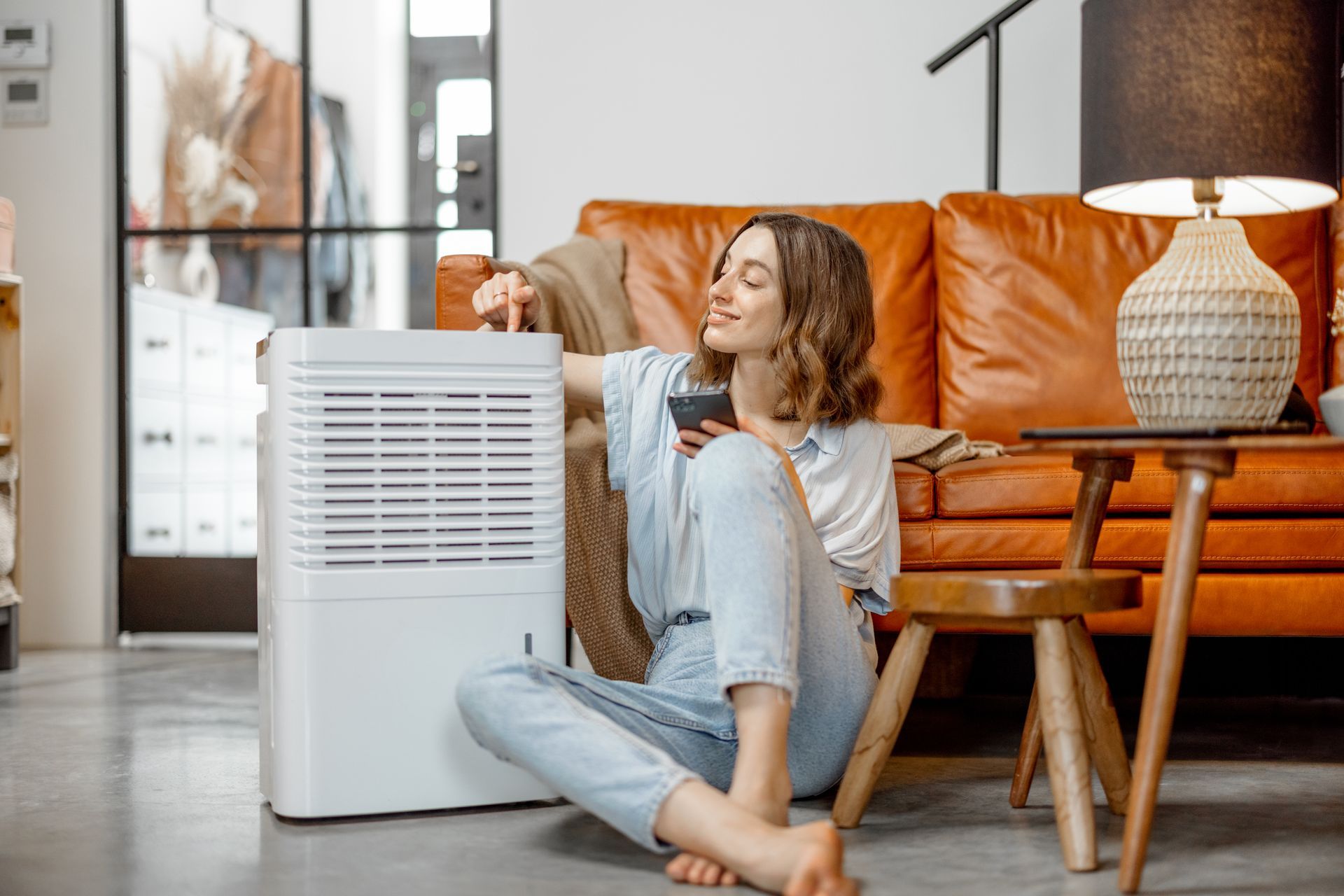 A woman is sitting on the floor in front of a humidifier in a living room.