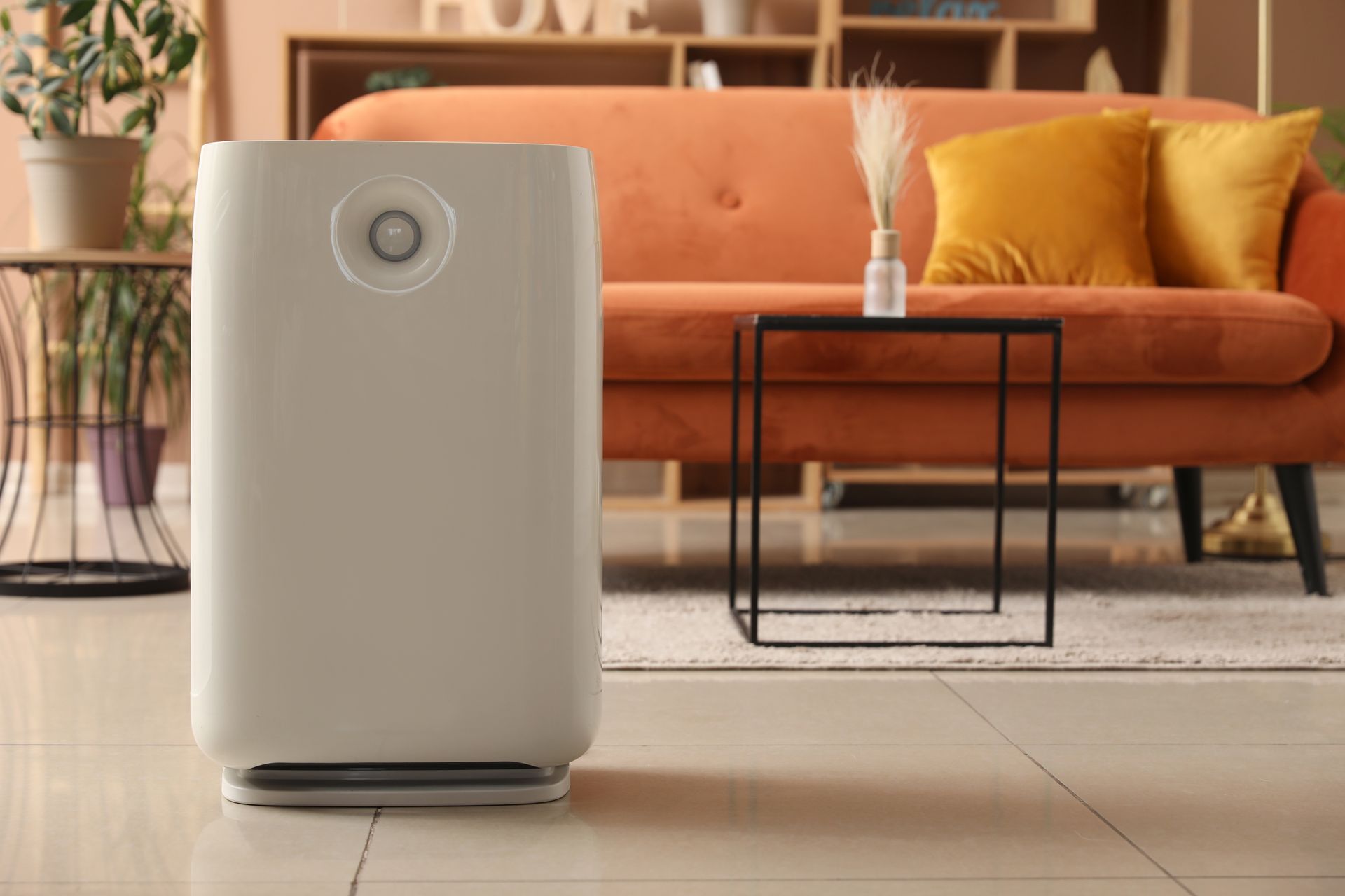 A white air purifier is sitting in a living room next to an orange couch.