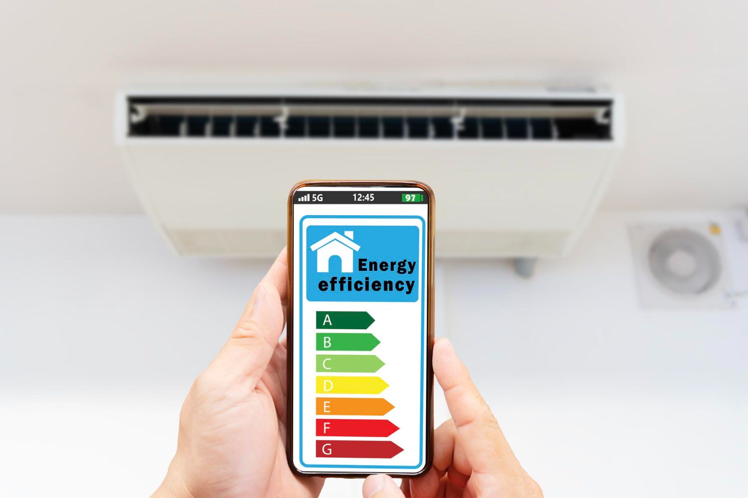 Hand holding phone showing energy efficiency chart in front of an air conditioner