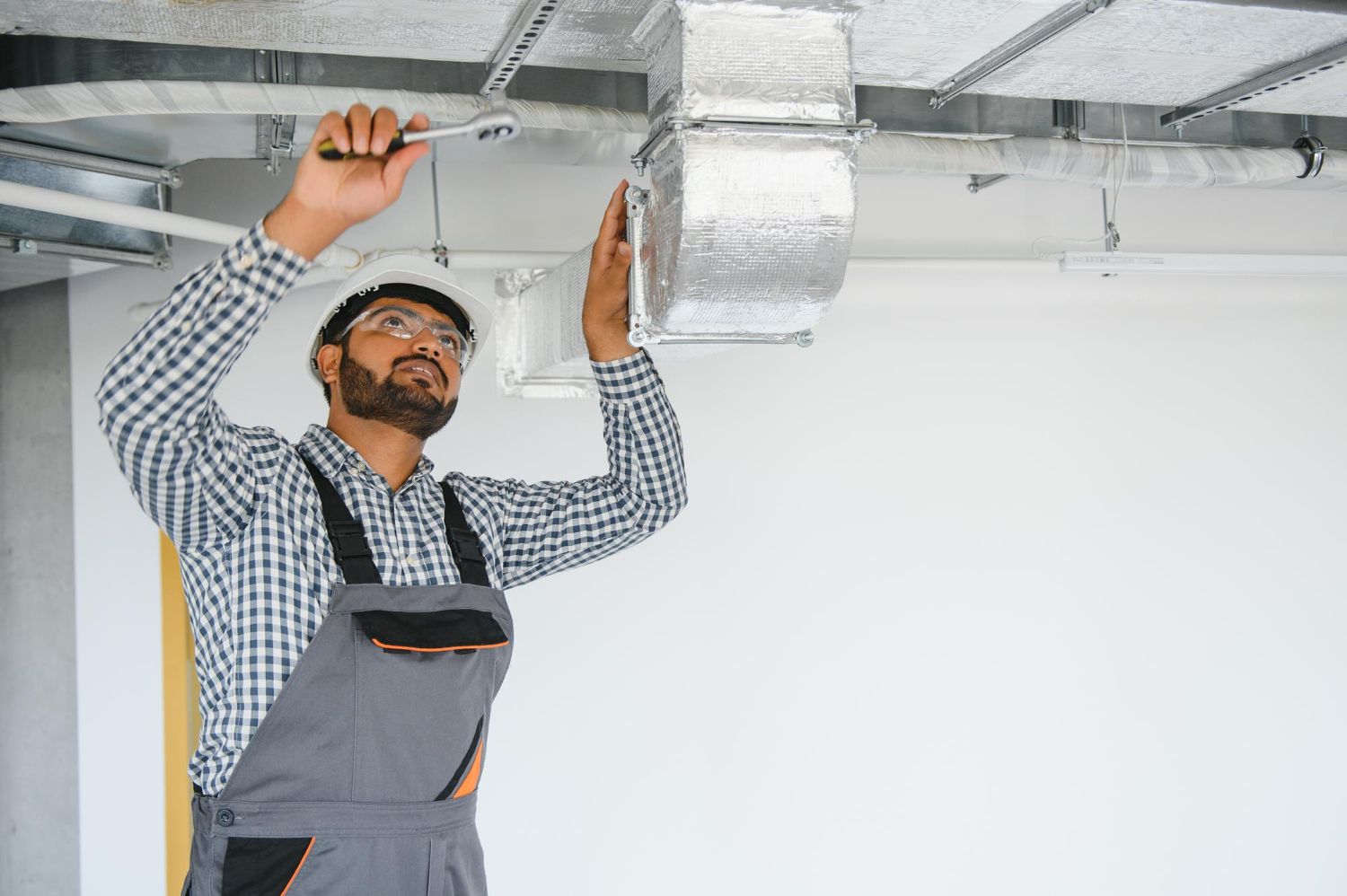 A man is fixing a ventilation system on the ceiling.