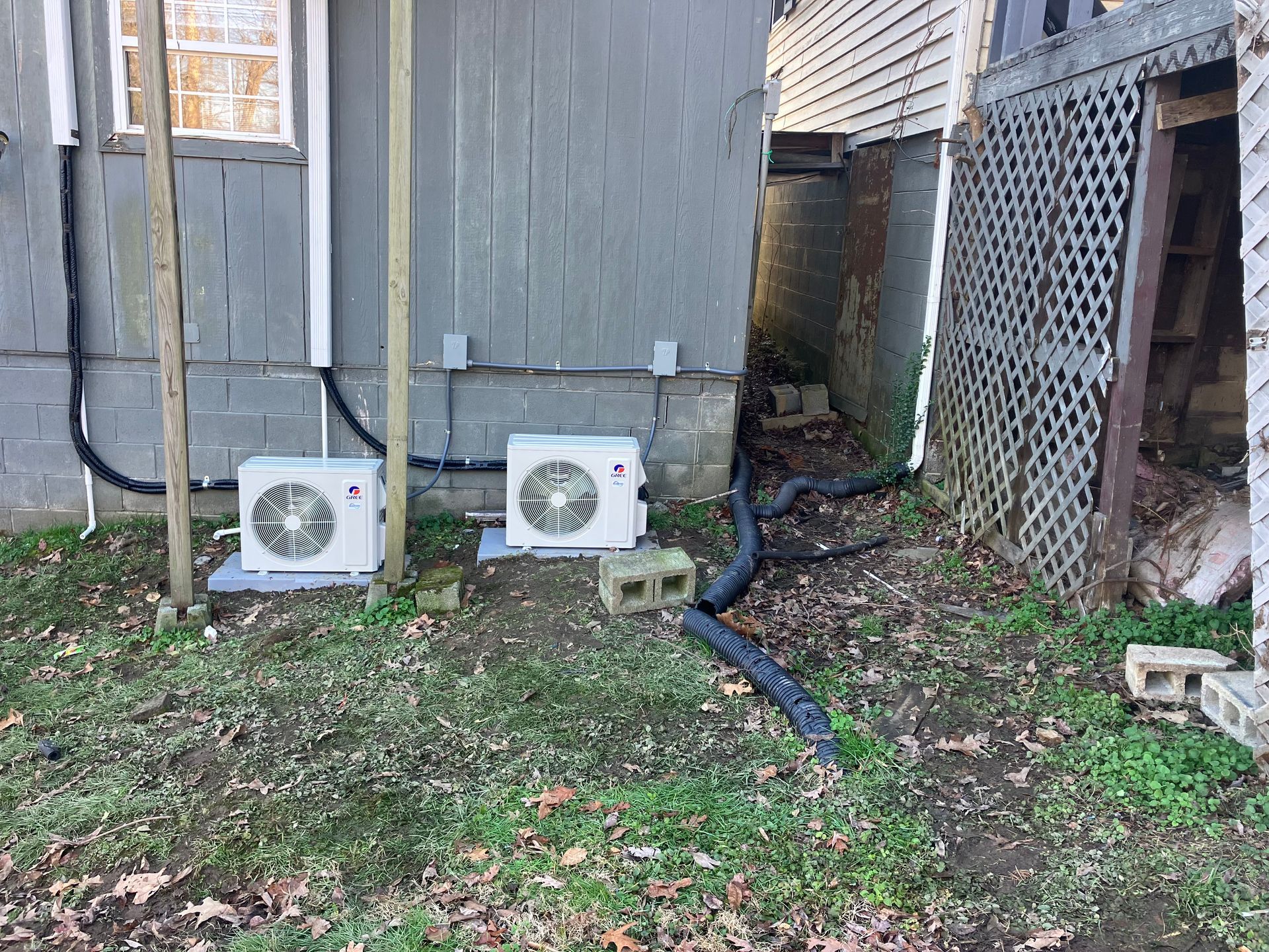 Two air conditioners are sitting outside of a house.