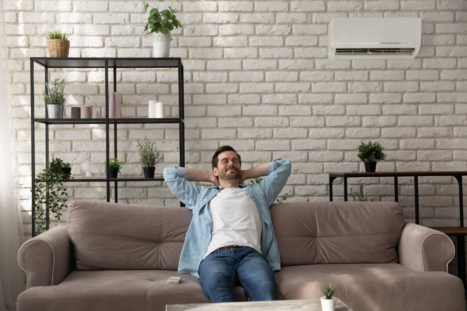 A man is sitting on a couch in a living room with his hands behind his head.