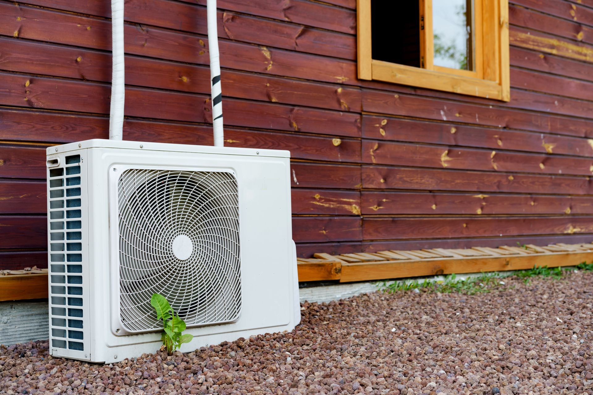 An air conditioning unit next to a brown wooden building.