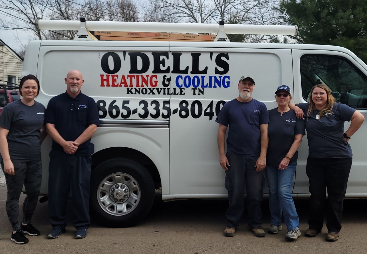 A group of people standing in front of a o dell 's heating and cooling van