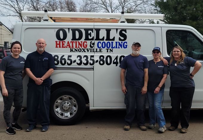 A group of people standing in front of a o dell 's heating and cooling van