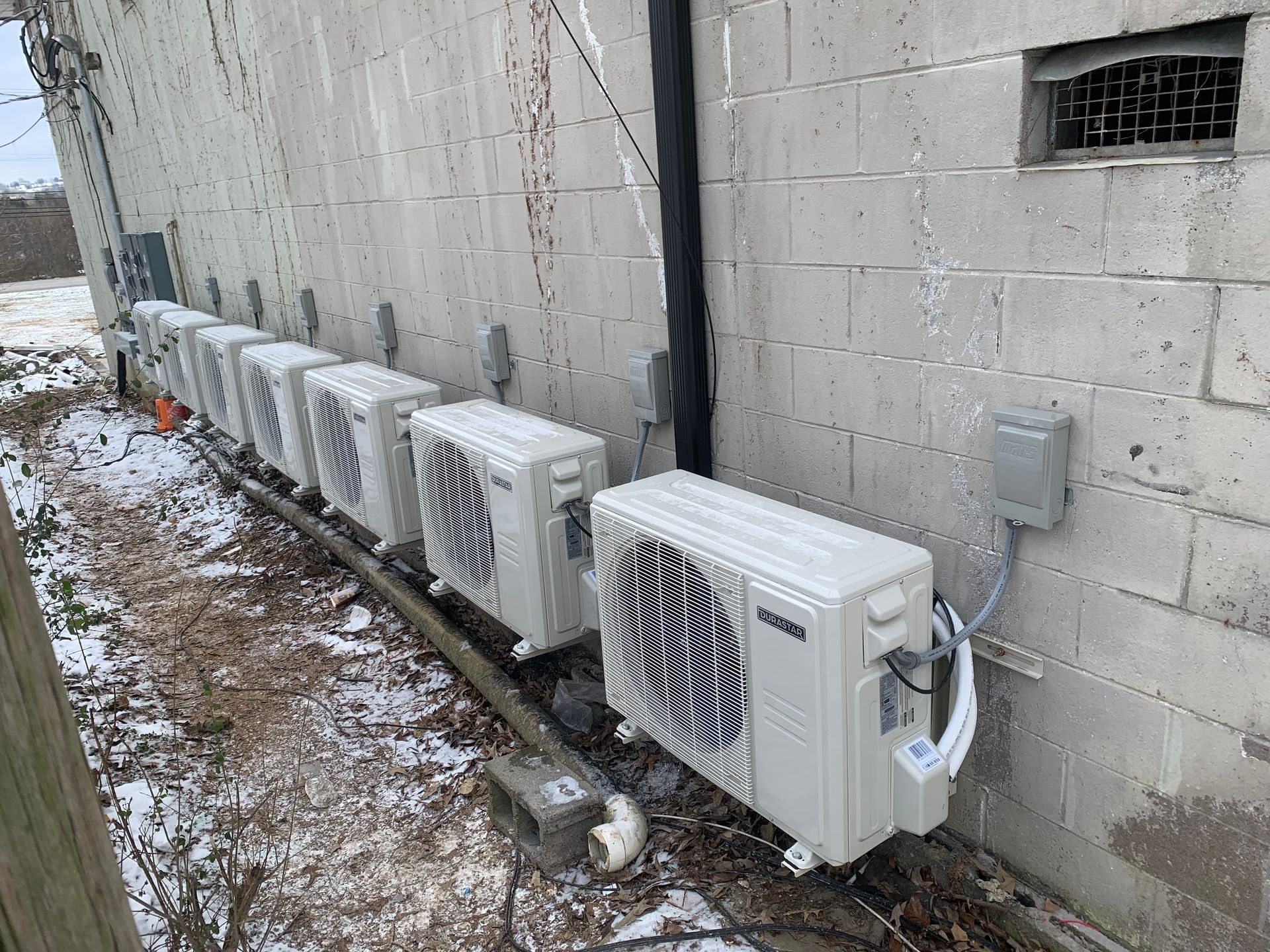 A row of air conditioners are lined up on the side of a building.