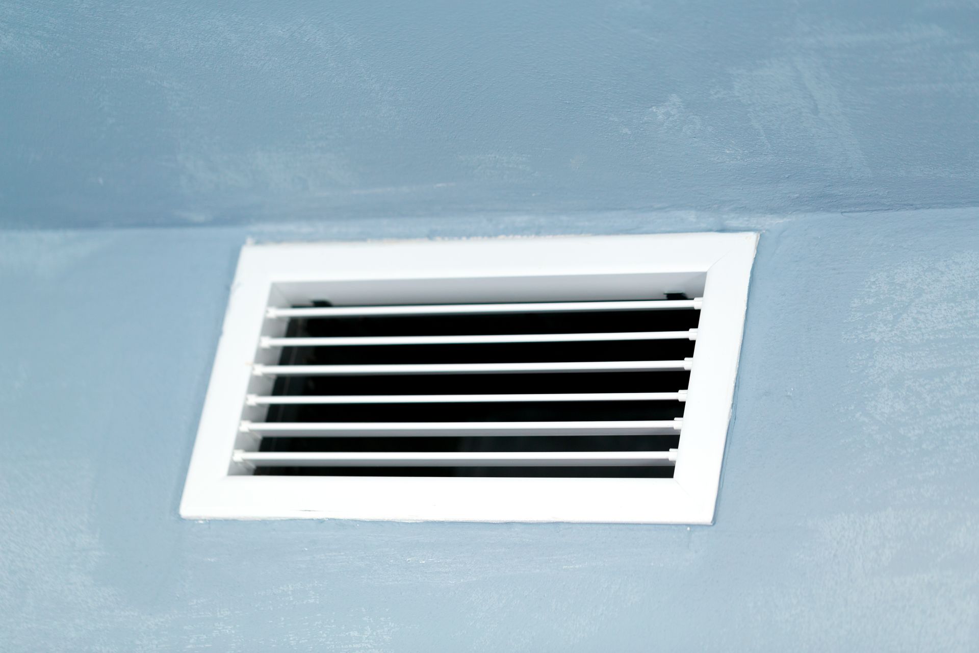 White rectangular vent on a light blue wall, with black slats.