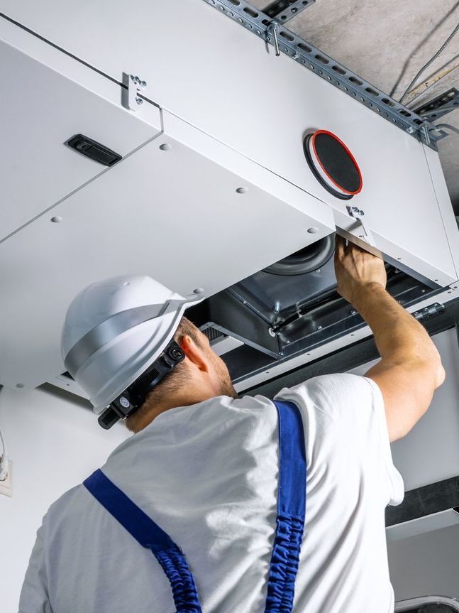 A man is working on a ventilation system in a building.