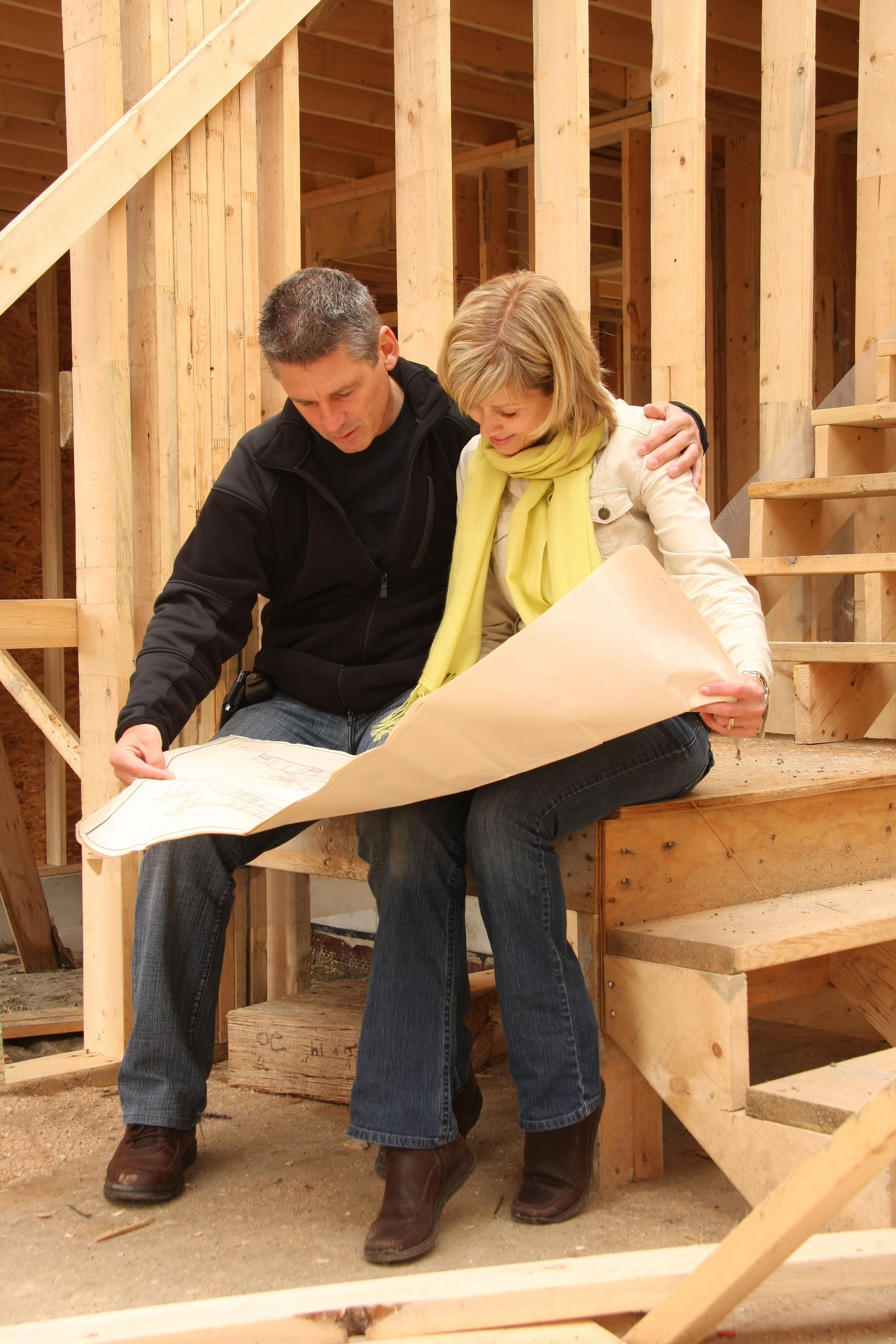 A man and a woman are sitting on stairs looking at a blueprint.