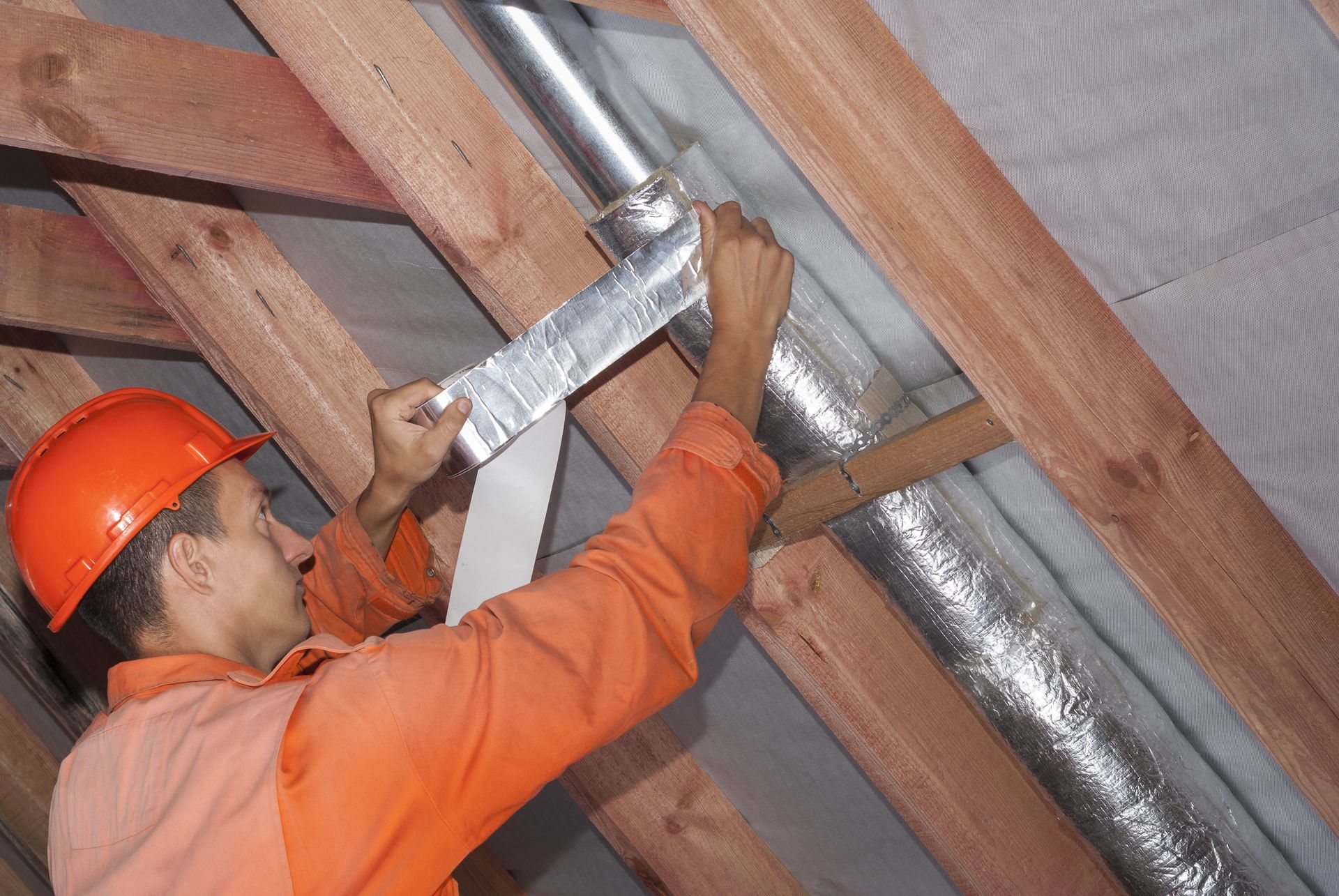 A man is working on a pipe in the attic.