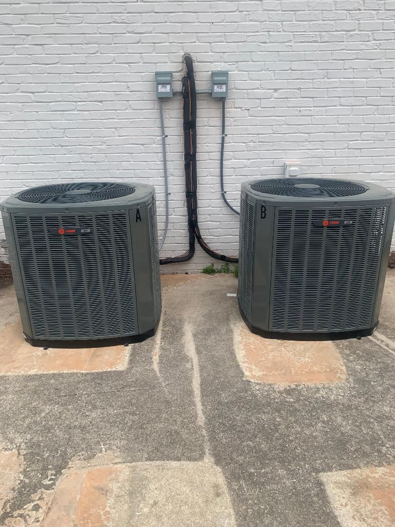 Two air conditioners are sitting next to each other in front of a white brick wall.
