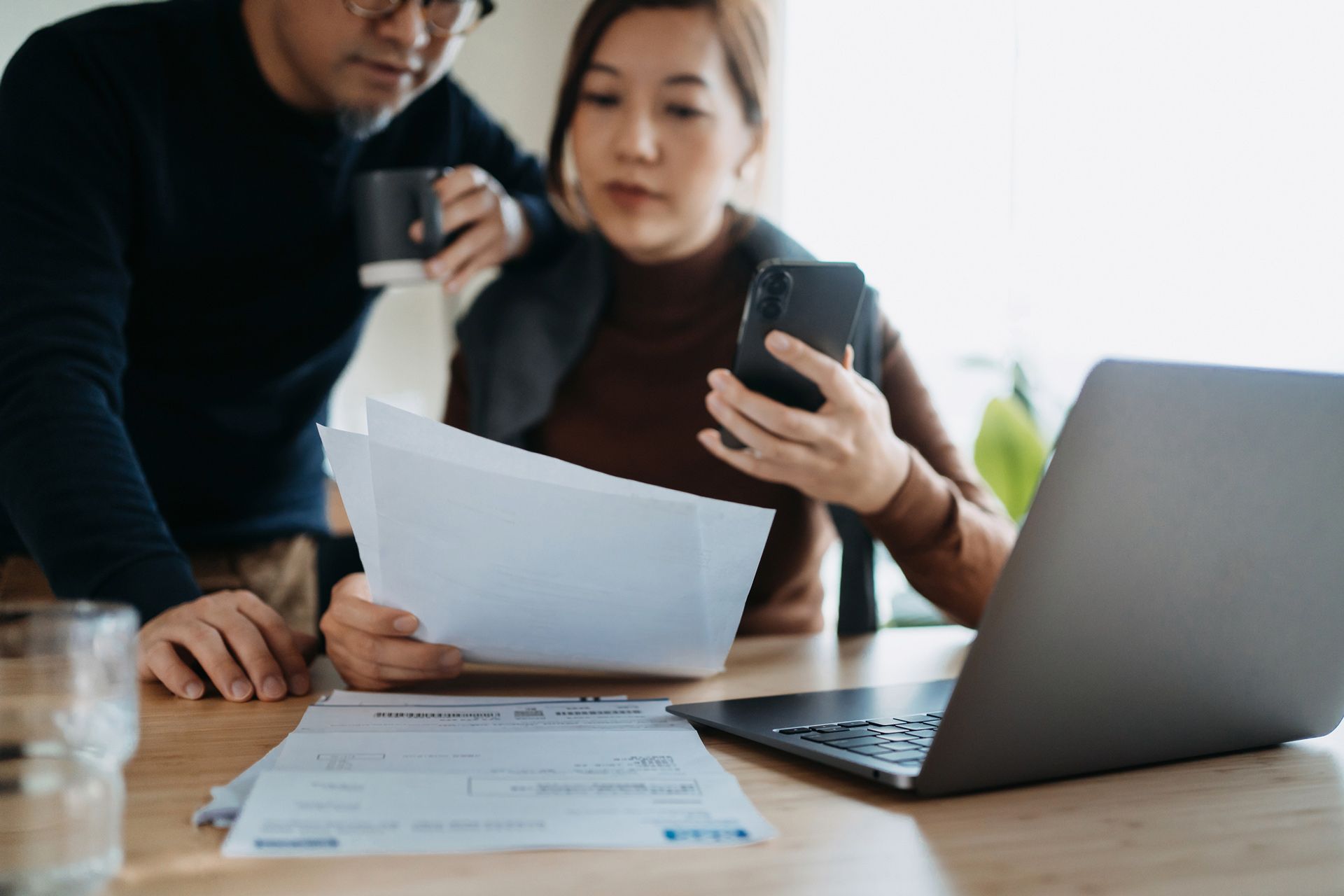 A man and a woman are sitting at a table looking at papers and a laptop.