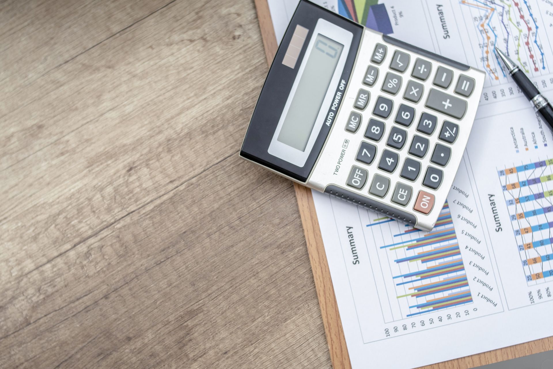 A calculator is sitting on top of a clipboard next to a magnifying glass.