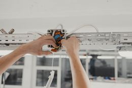Person wiring electrical box on ceiling.