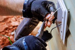 Hands in gloves working on electrical wiring with pliers.