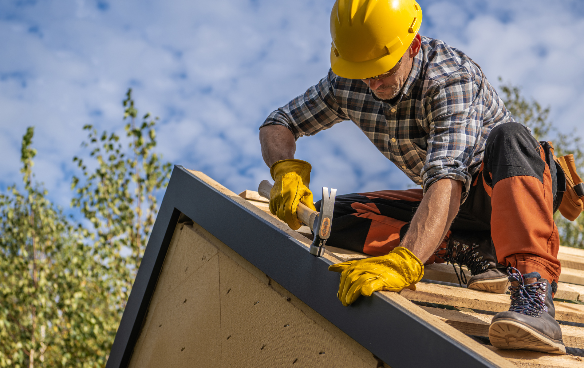 A man wearing a hard hat is working on a roof.