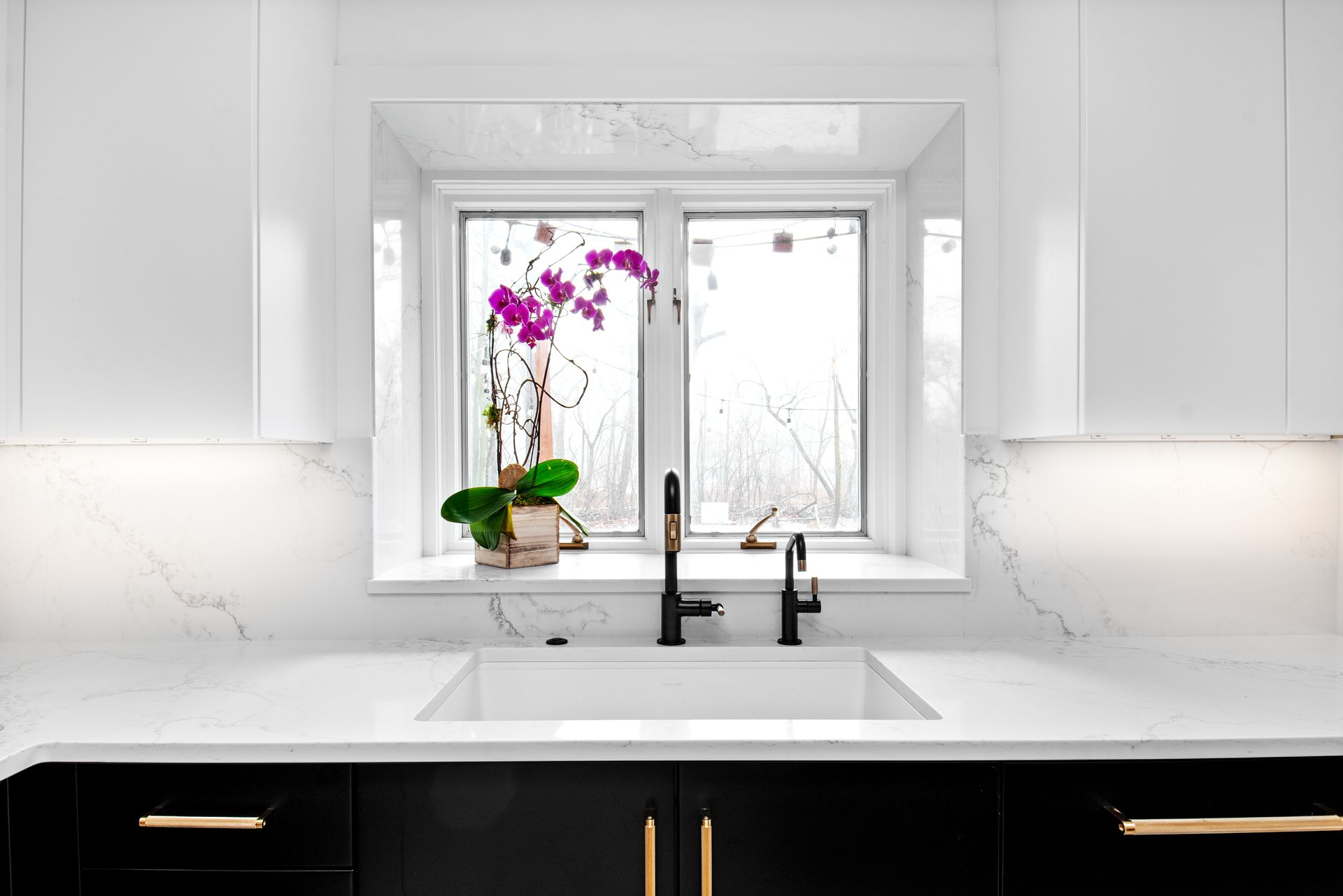 A kitchen sink in front of a window with a potted plant on the window sill.