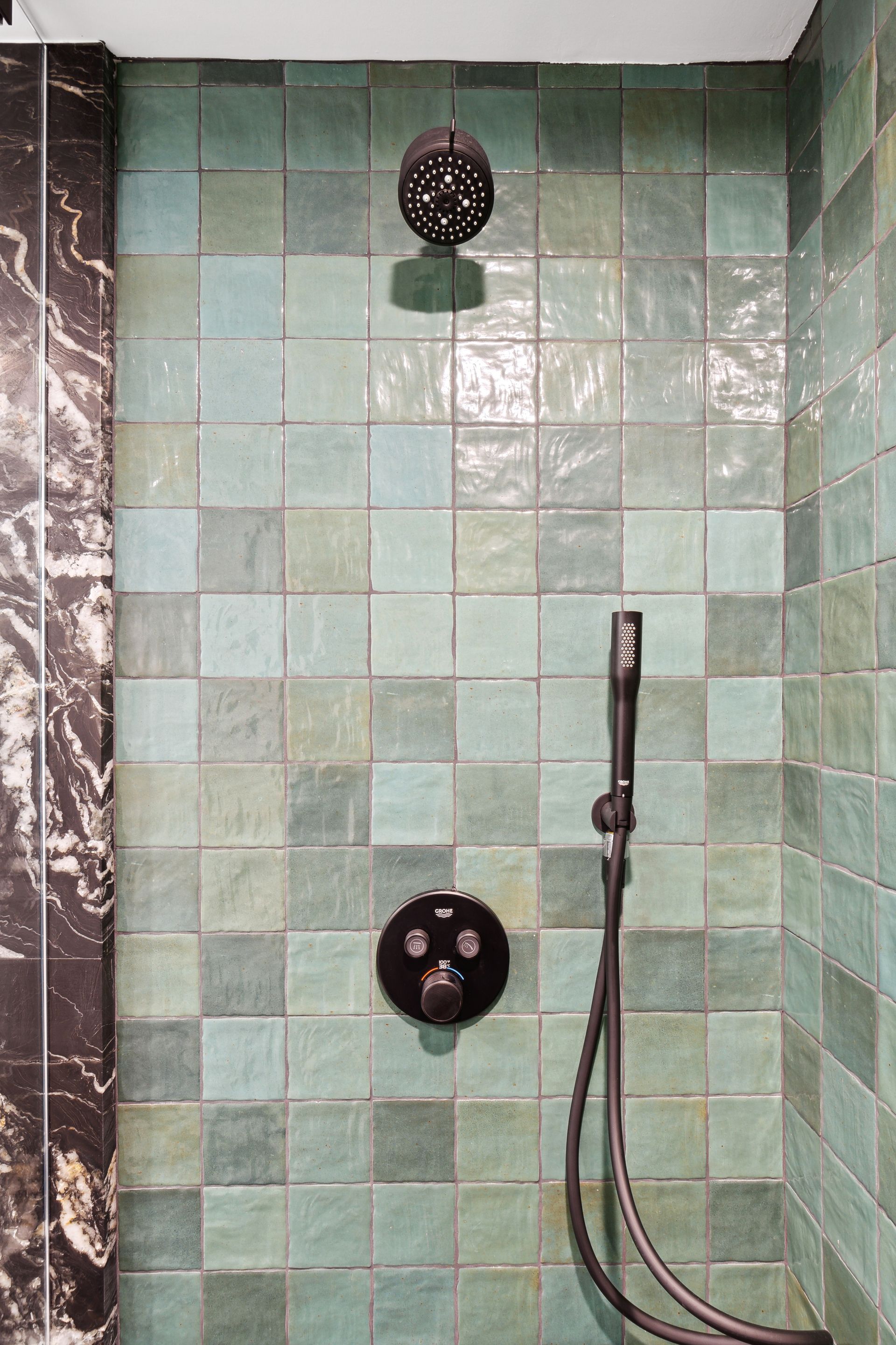 A shower with green tiles and a black shower head.