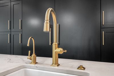 A kitchen sink with two gold faucets and black cabinets.