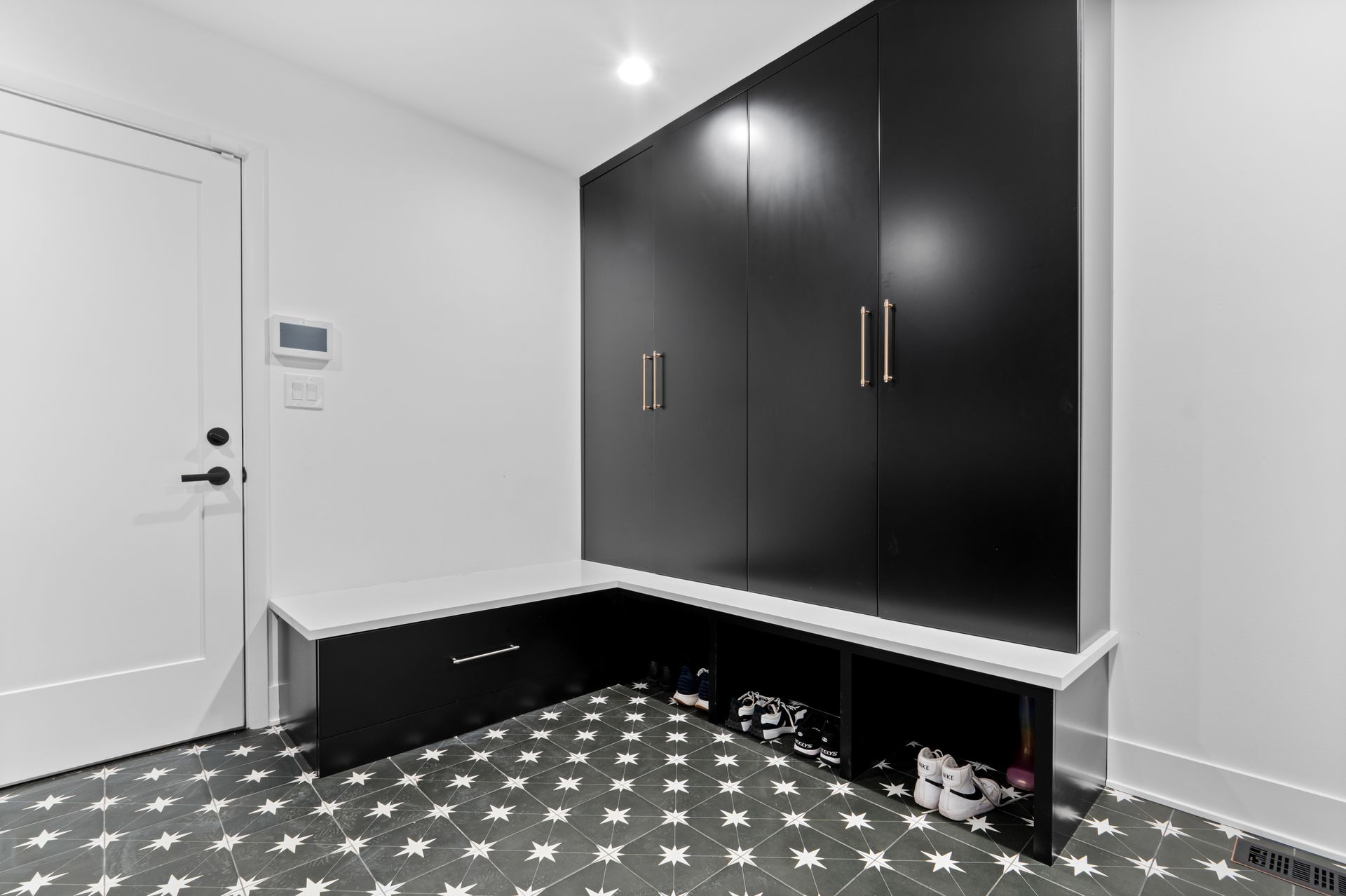 A black and white photo of a hallway with black cabinets and a bench.