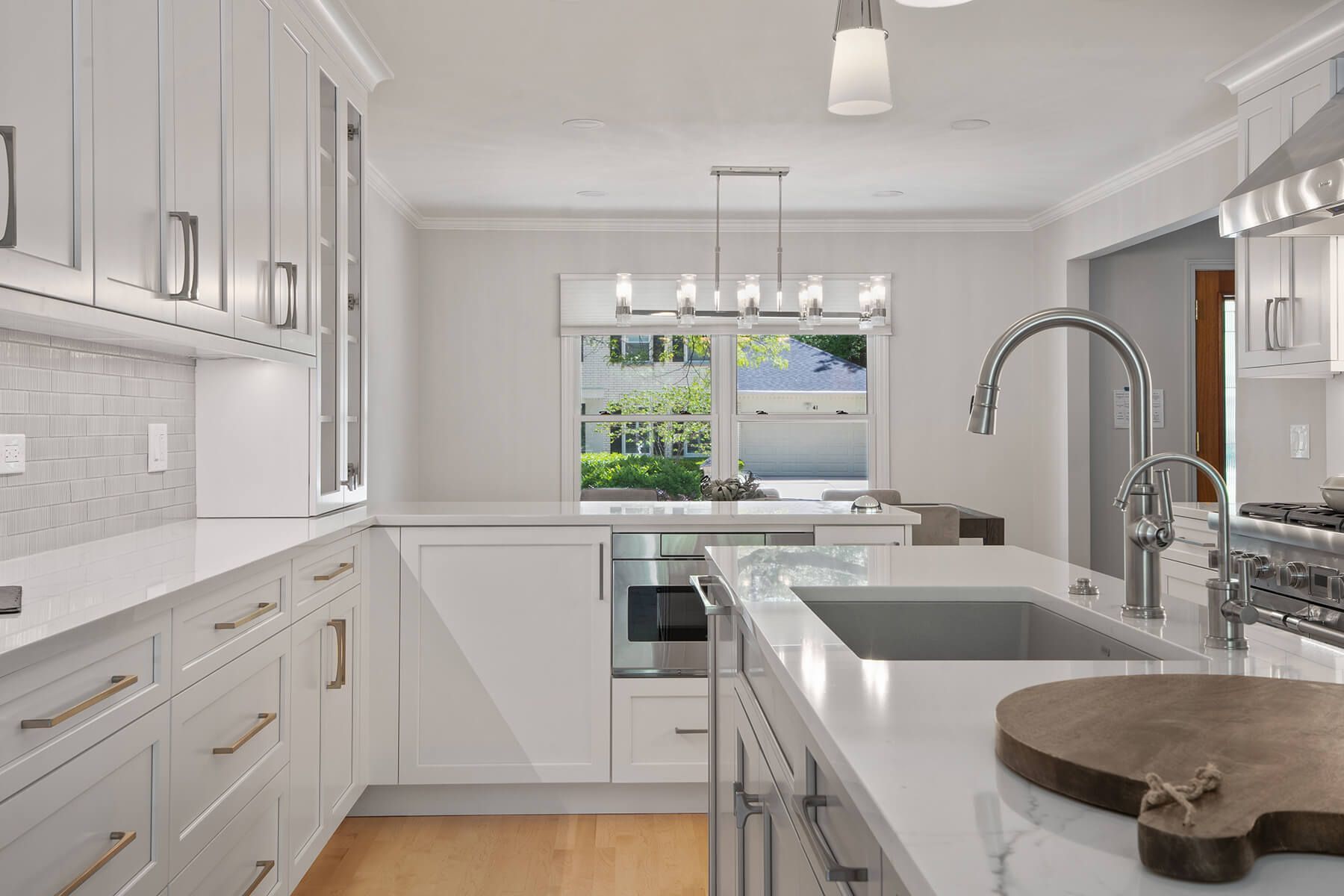 A kitchen with white cabinets , a sink , a cutting board and a window.