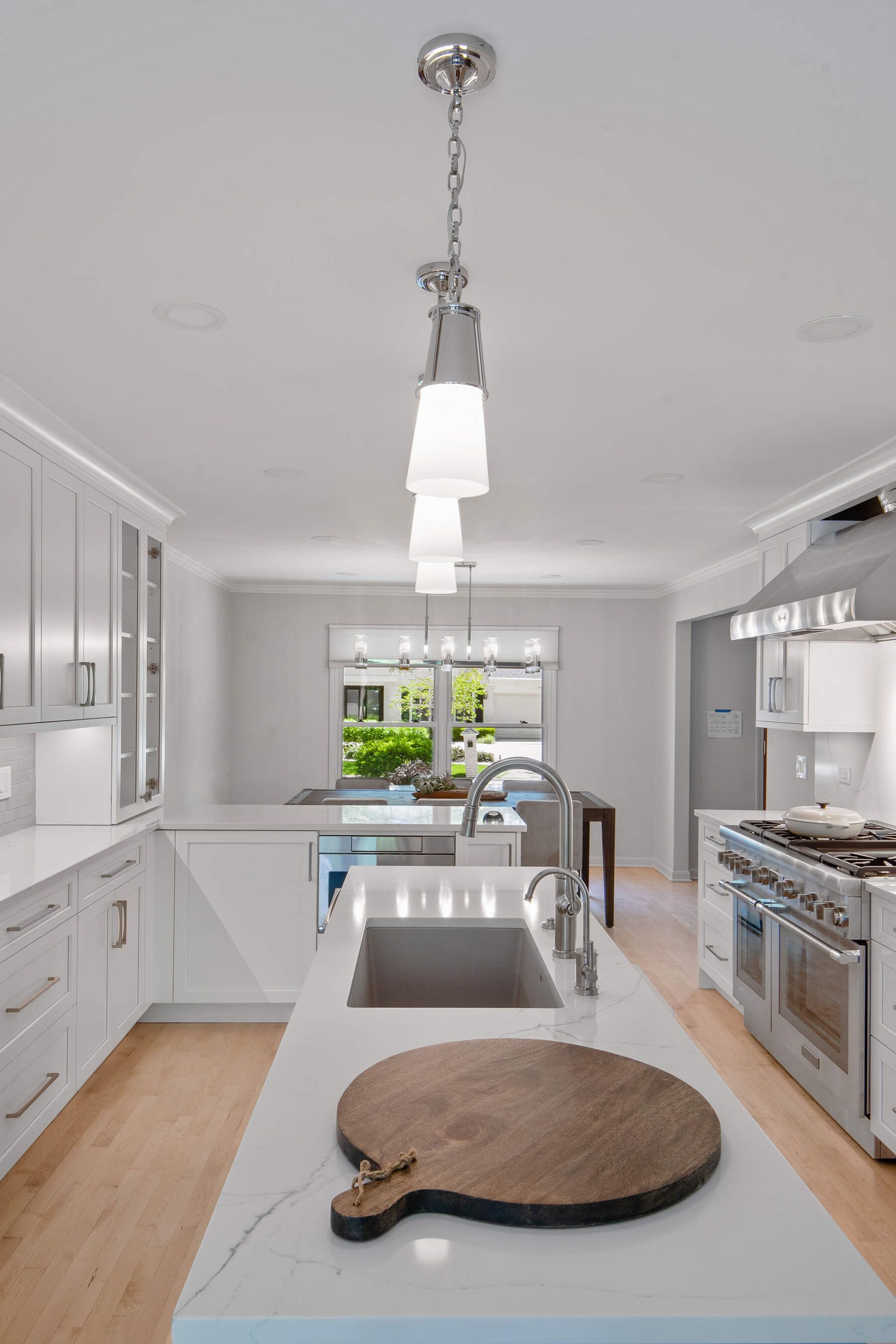 A kitchen with white cabinets and stainless steel appliances and a wooden cutting board on the counter.